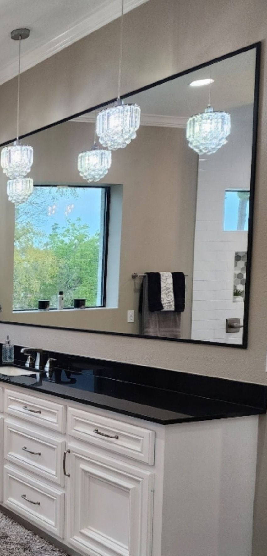 Modern bathroom vanity with a black countertop, white cabinets, and a large, black-framed mirror reflecting pendant lights.
