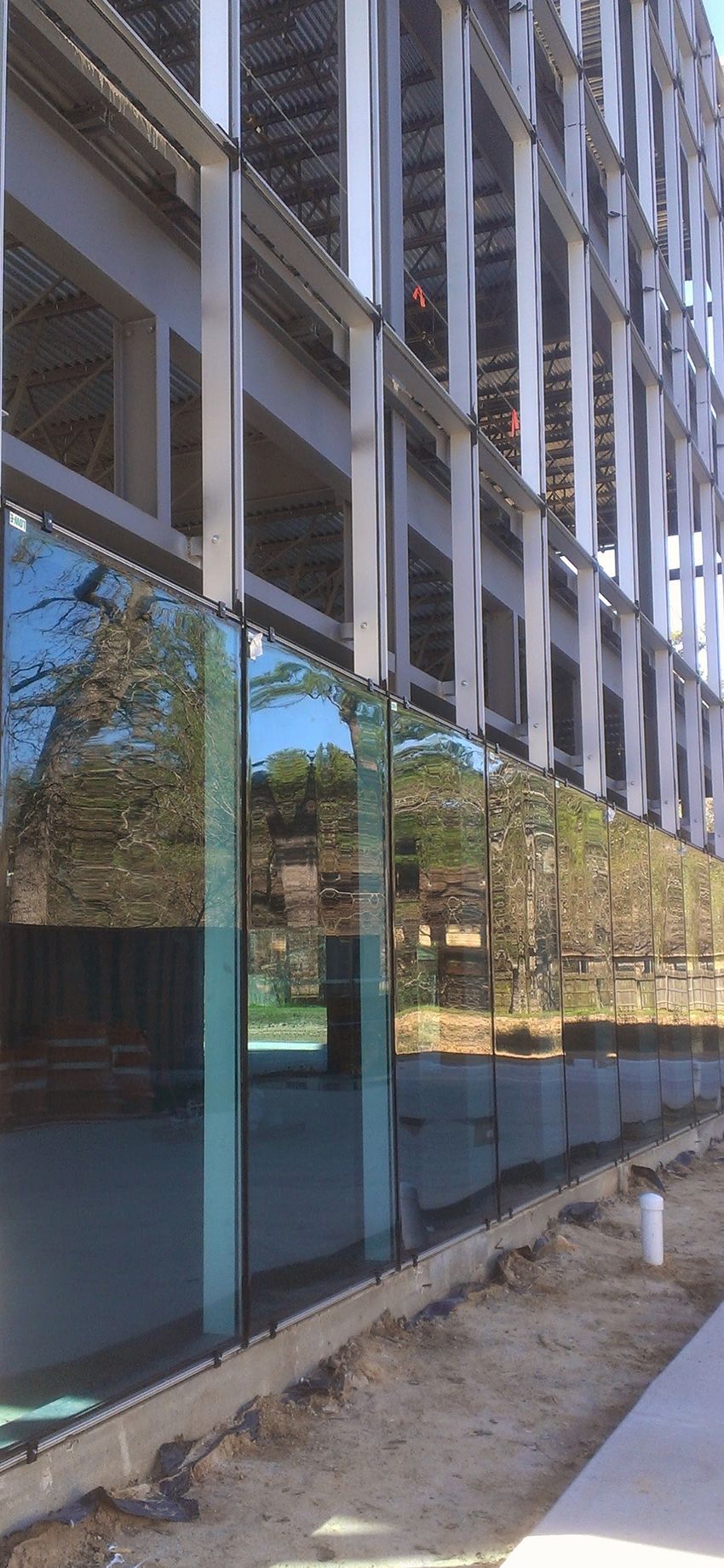 A construction site showing glass panels installed on the lower facade of a building with an exposed steel frame above.