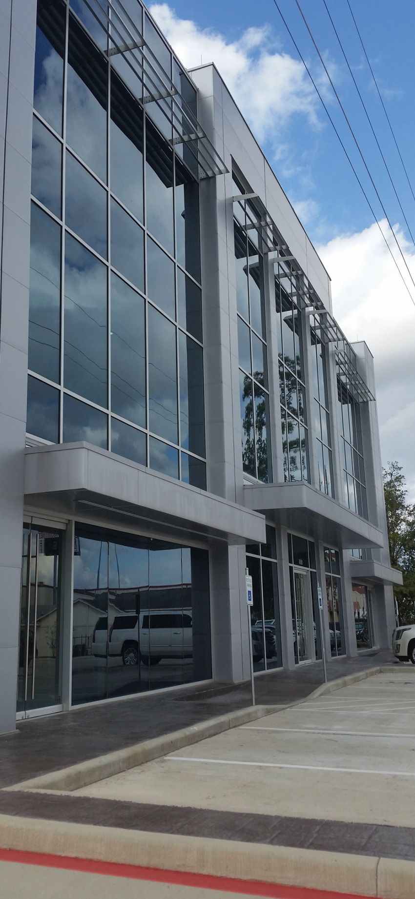 A modern, multi-story building featuring extensive glass curtain walls, gray concrete accents, and a ground-level entrance.