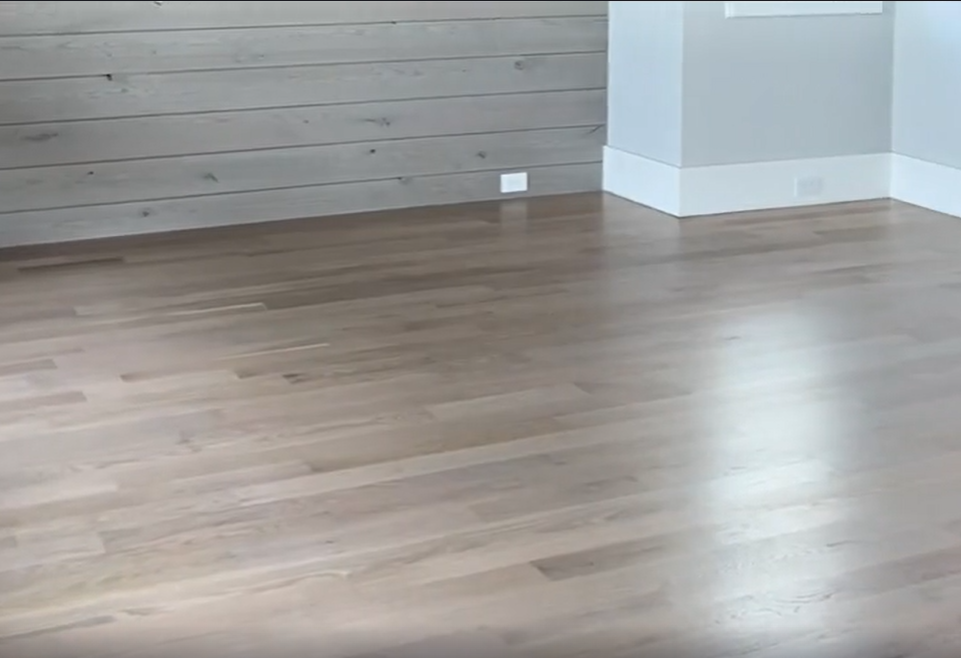 Empty modern room with light wood flooring, wood accent wall, and white walls and baseboards
