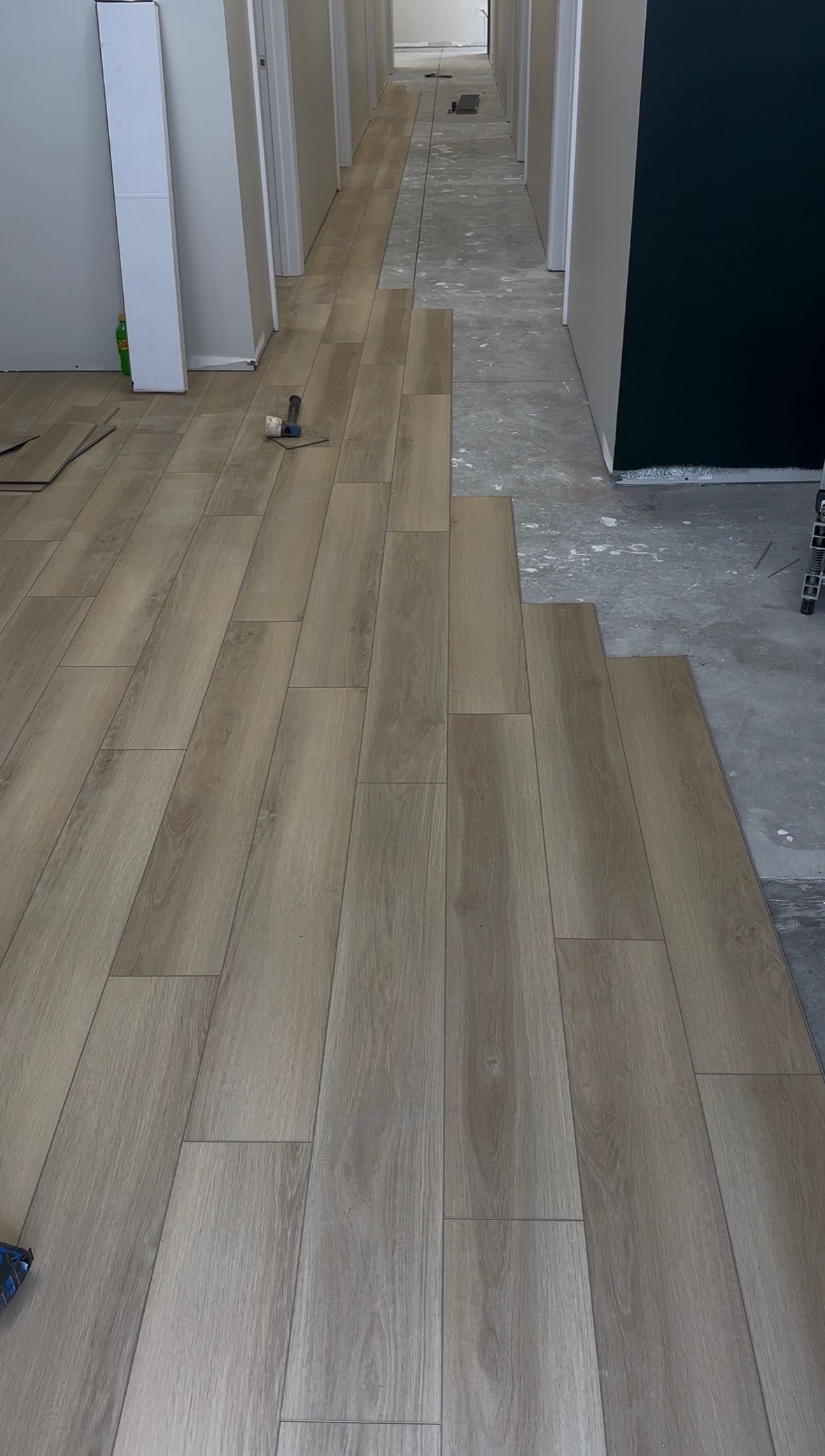 Wood flooring laid in a hallway beside unfinished concrete and white walls.