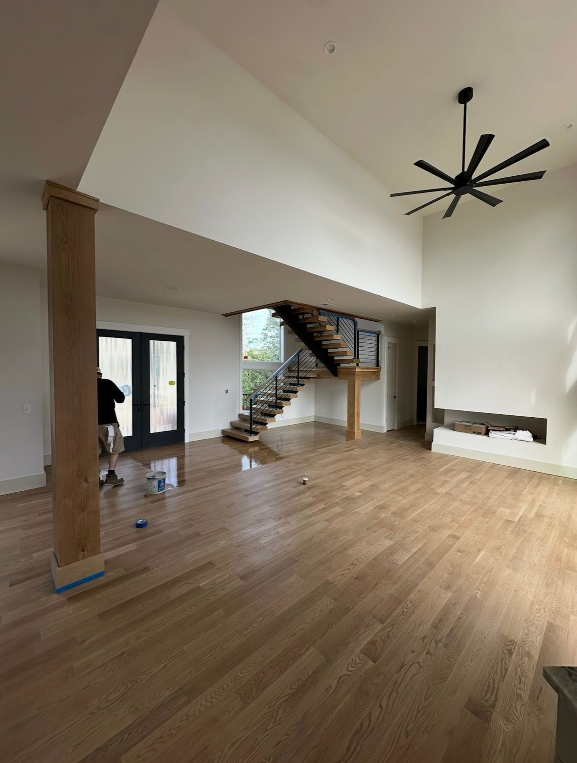 Spacious modern living room with wood floors, staircase, white walls, and a black ceiling fan