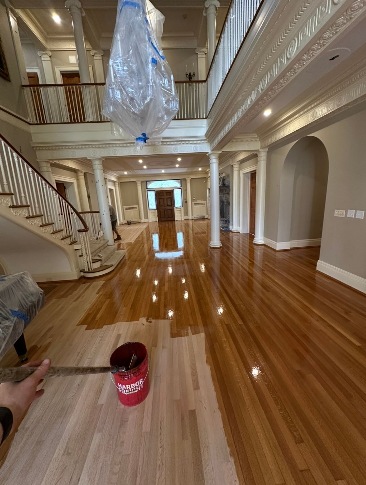 Grand foyer with glossy hardwood floor under refinishing, staircase, chandelier, and wrapped light fixture hanging above