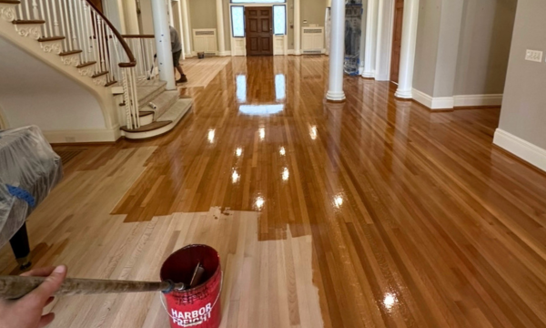Shiny hardwood foyer with staircase, white columns, and a red bucket in the foreground.