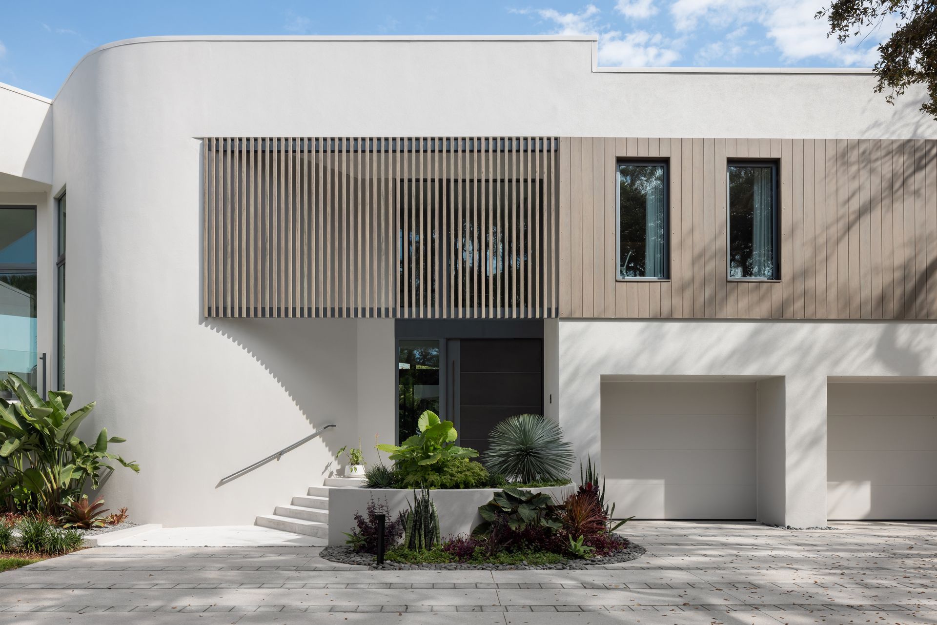 Modern white house with wooden accents and landscaping, including a curved wall and garage.