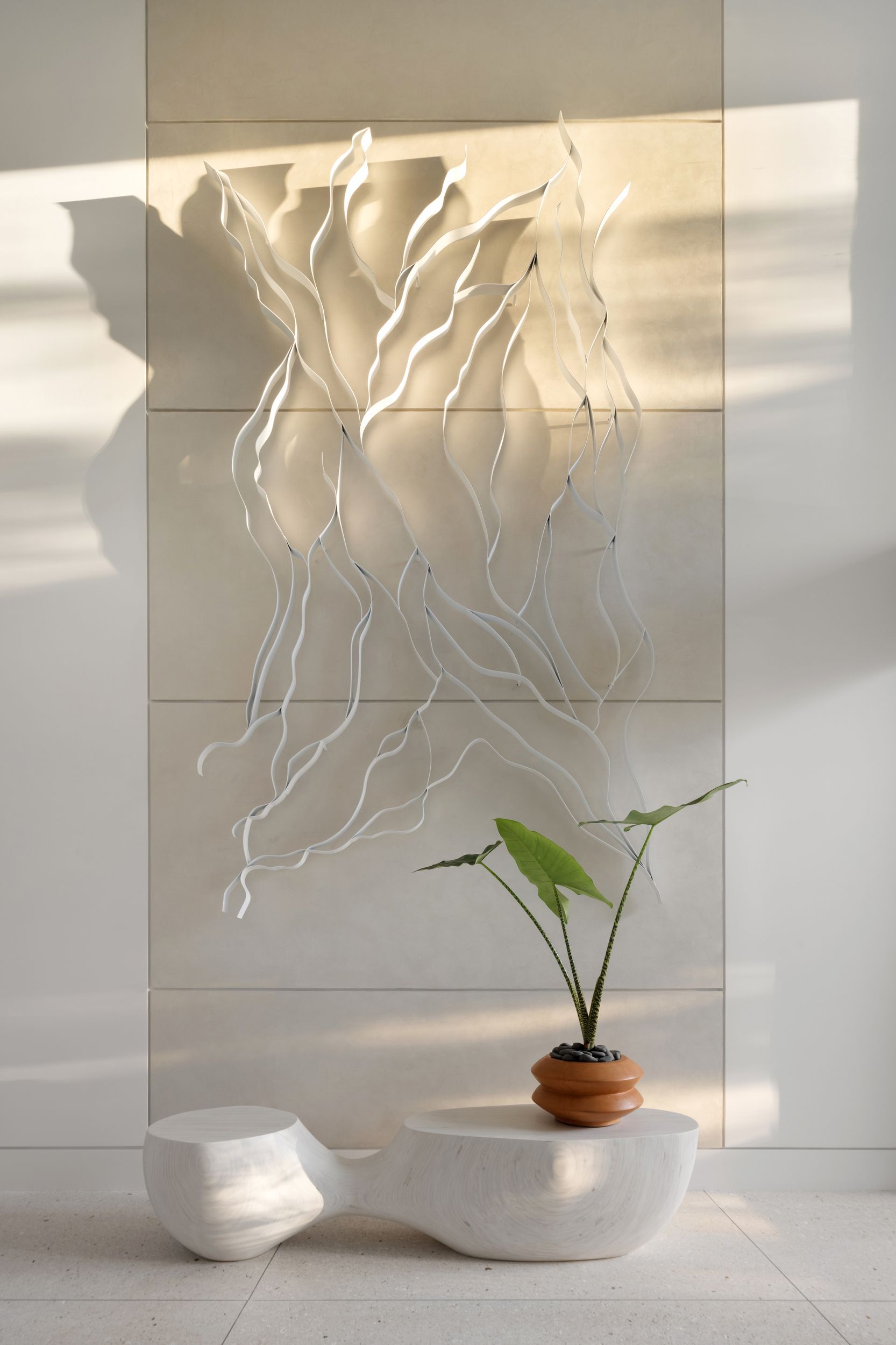 White wall art over a minimalist table with a plant. Bright, sunny room.