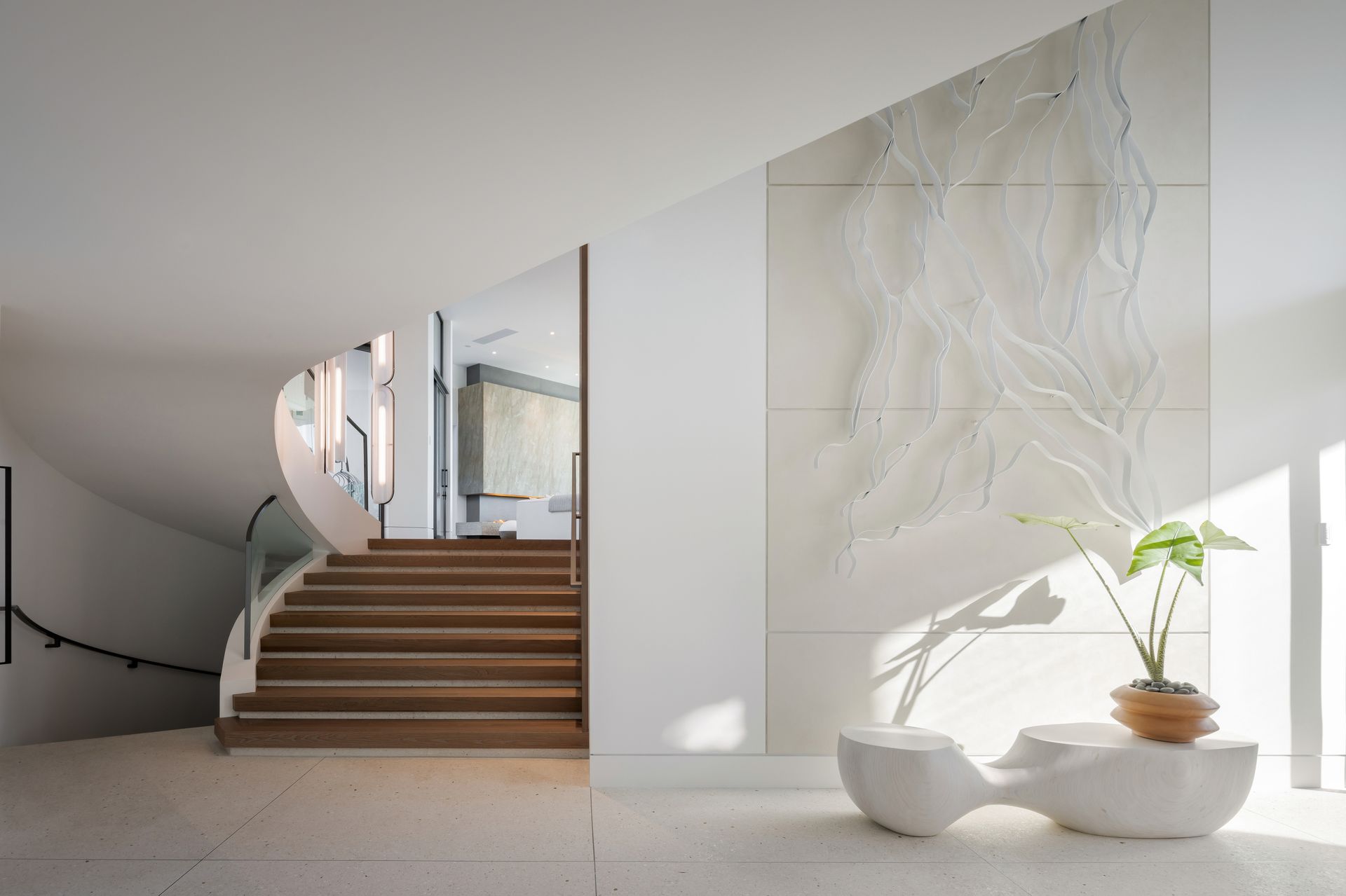 Modern white interior with a curved staircase, wood steps, and abstract wall art.
