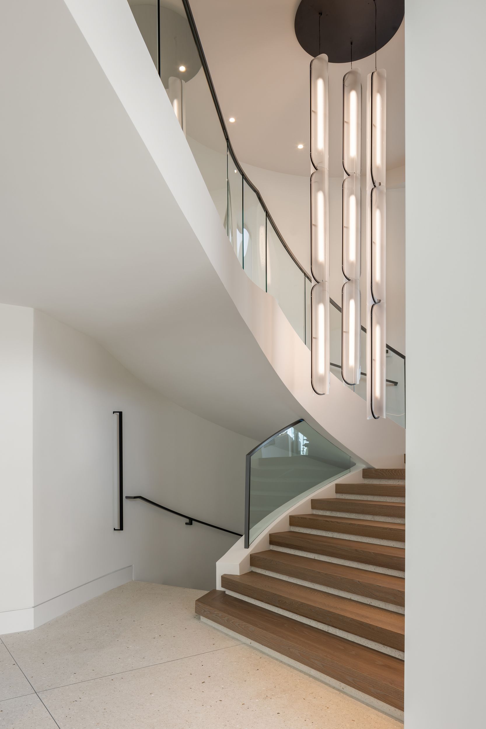 Curving staircase with glass railing, tan carpeted steps, and a modern light fixture.