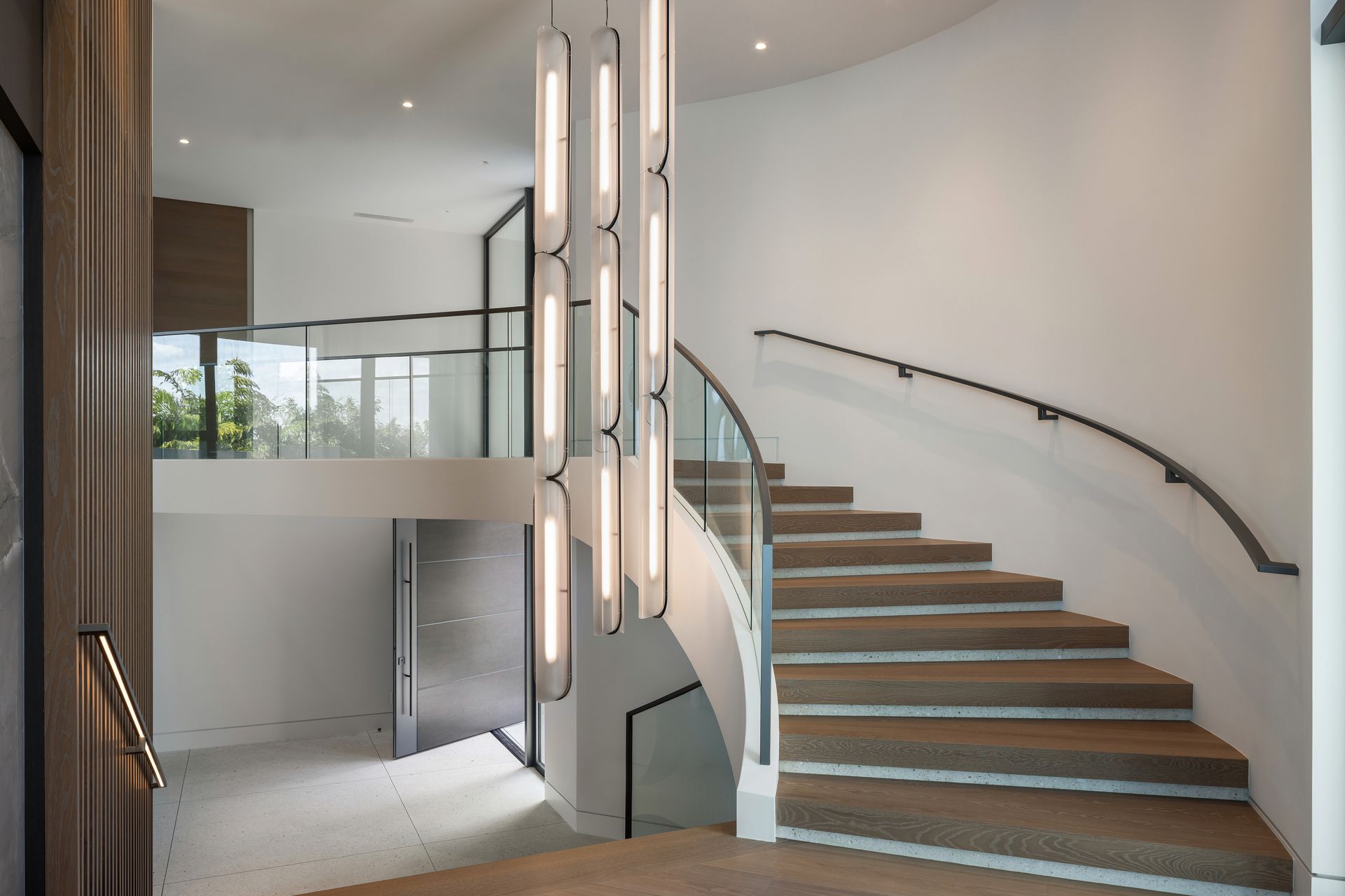 Elegant, modern entryway with a curved staircase, overhead chandelier, and a second-floor walkway.