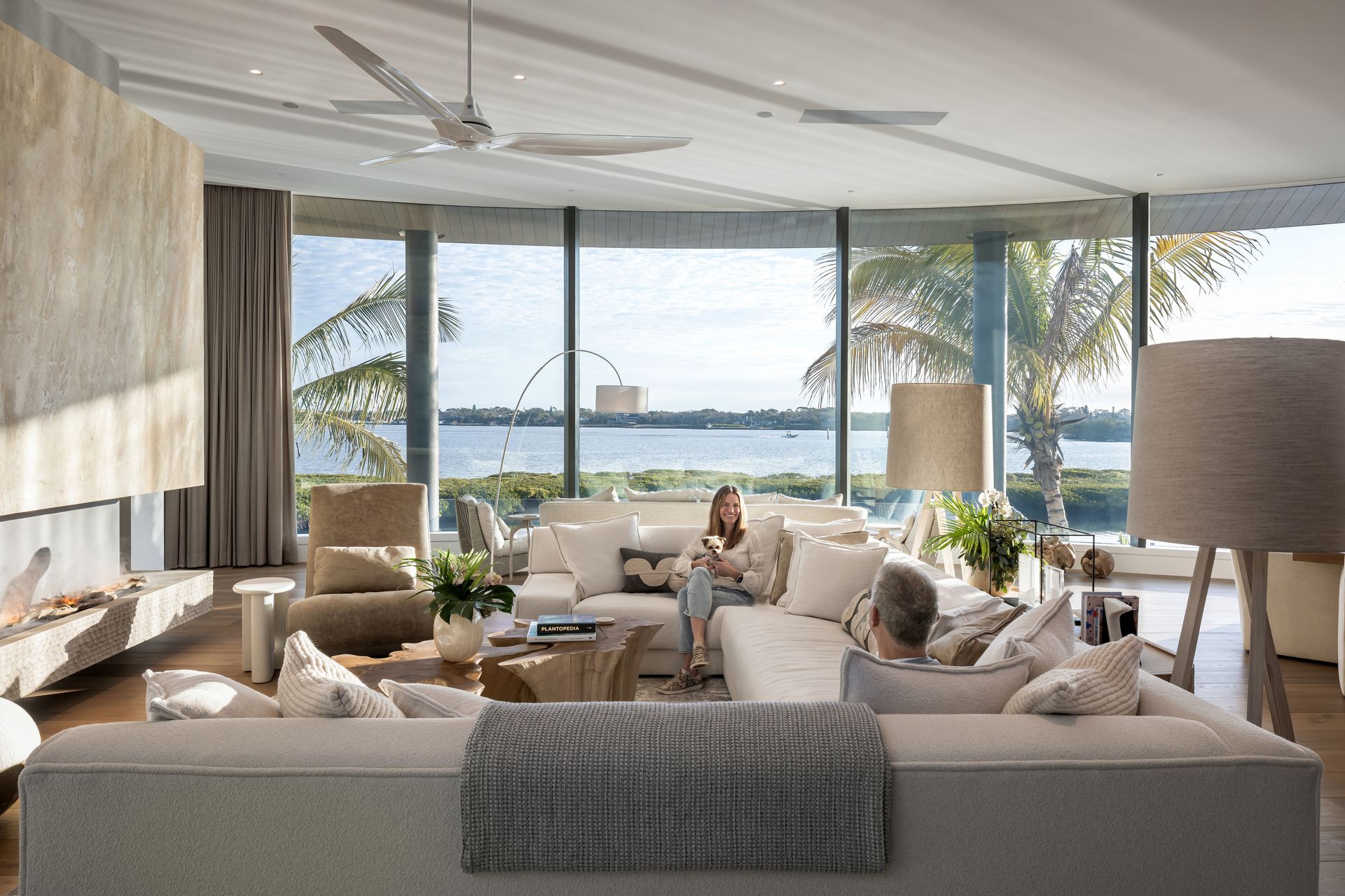 Spacious living room with waterfront view, featuring a woman on the sofa and a cozy atmosphere.