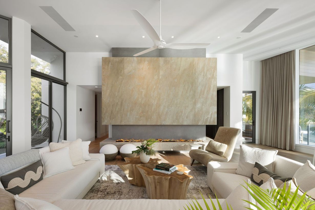 Modern living room with fireplace, white sofas, wooden coffee table, large windows.