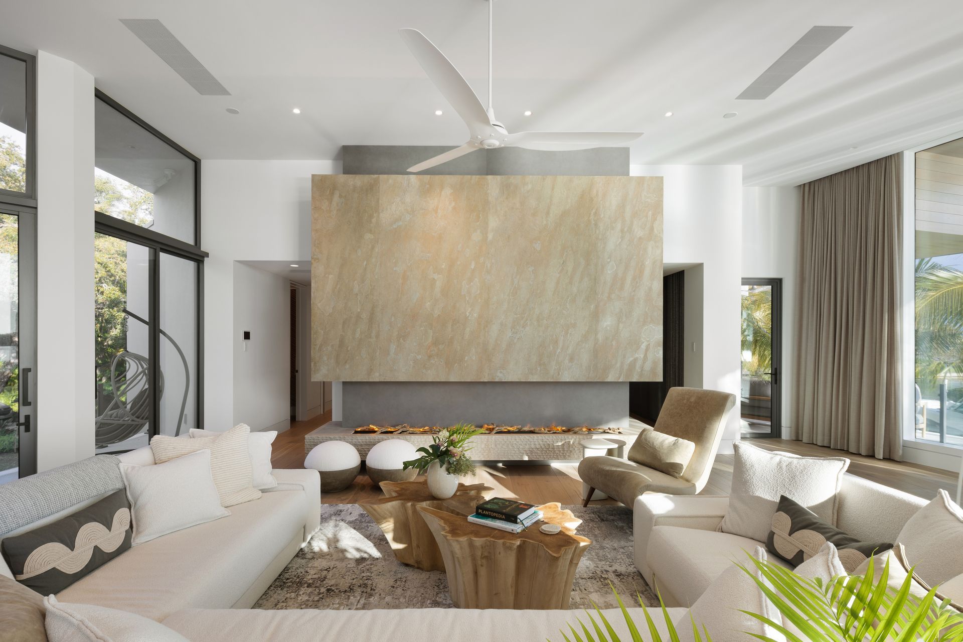 Modern living room with fireplace, white sofas, wooden coffee table, large windows.