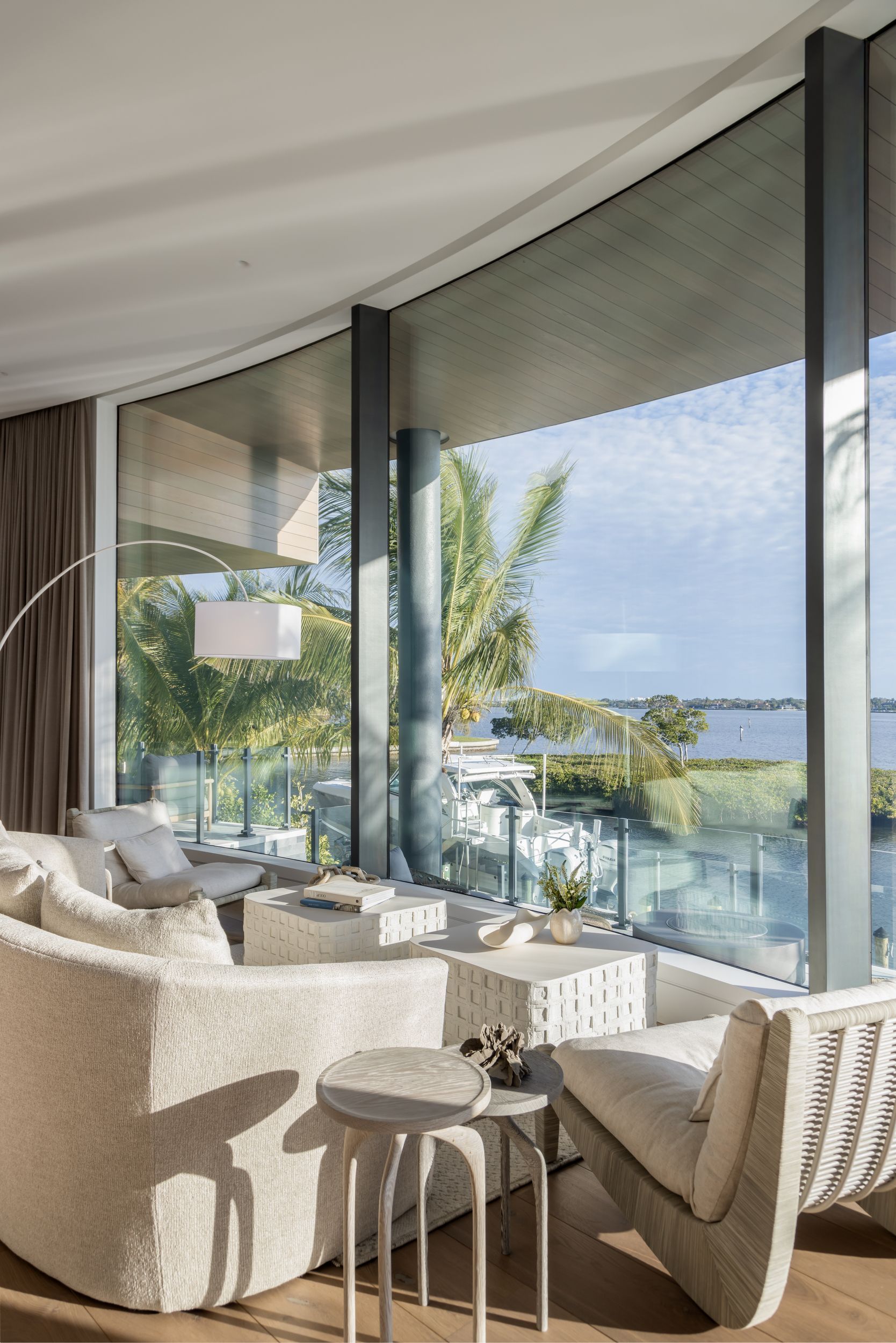 Living room with curved window overlooking water and trees; white sofa, chair, and side tables.