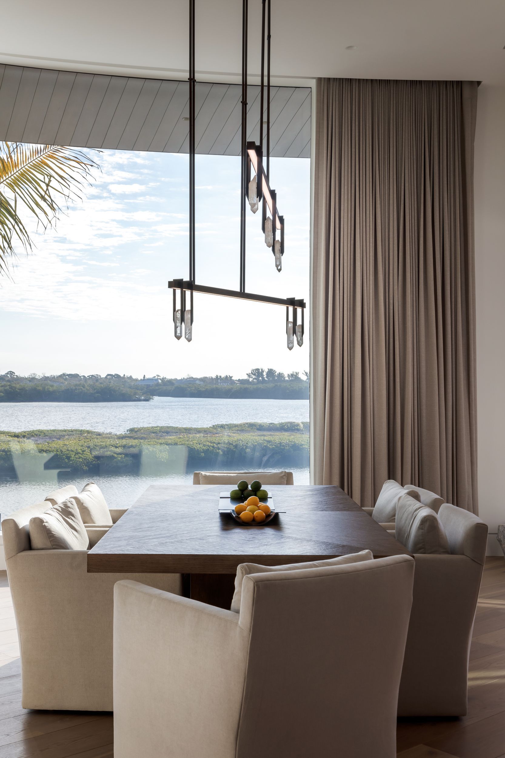 Dining room with large window, table, chairs, and modern light fixture; overlooking a river.