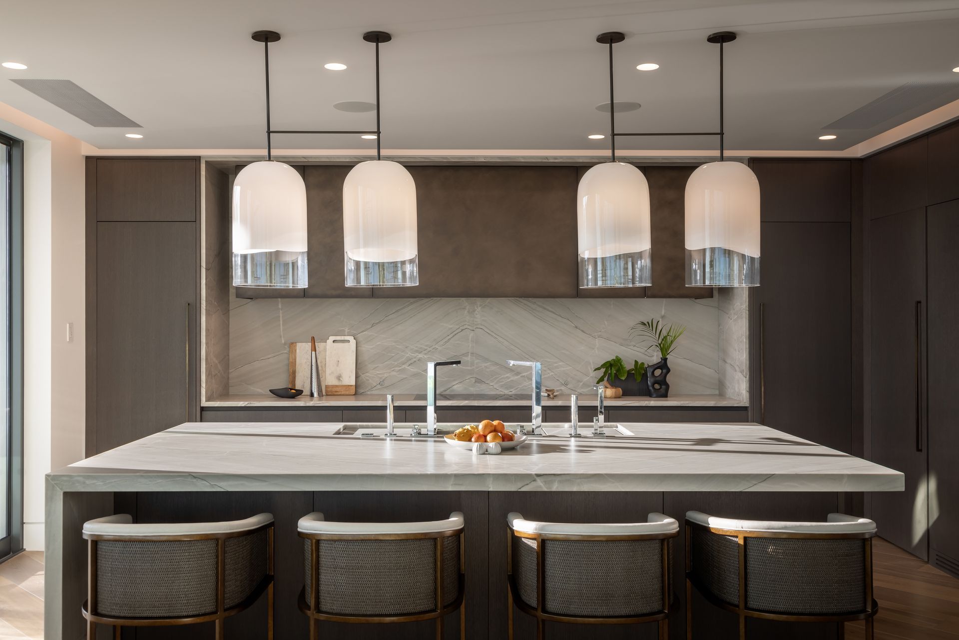 Modern kitchen with island, pendant lights, and gray cabinets. Four barstools are in front of the island.