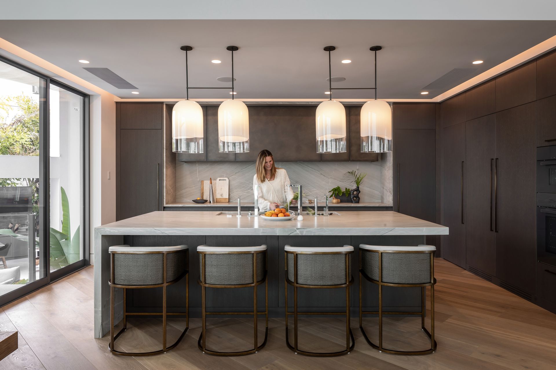 Modern kitchen with dark cabinetry, large island, pendant lights, and person at the counter.