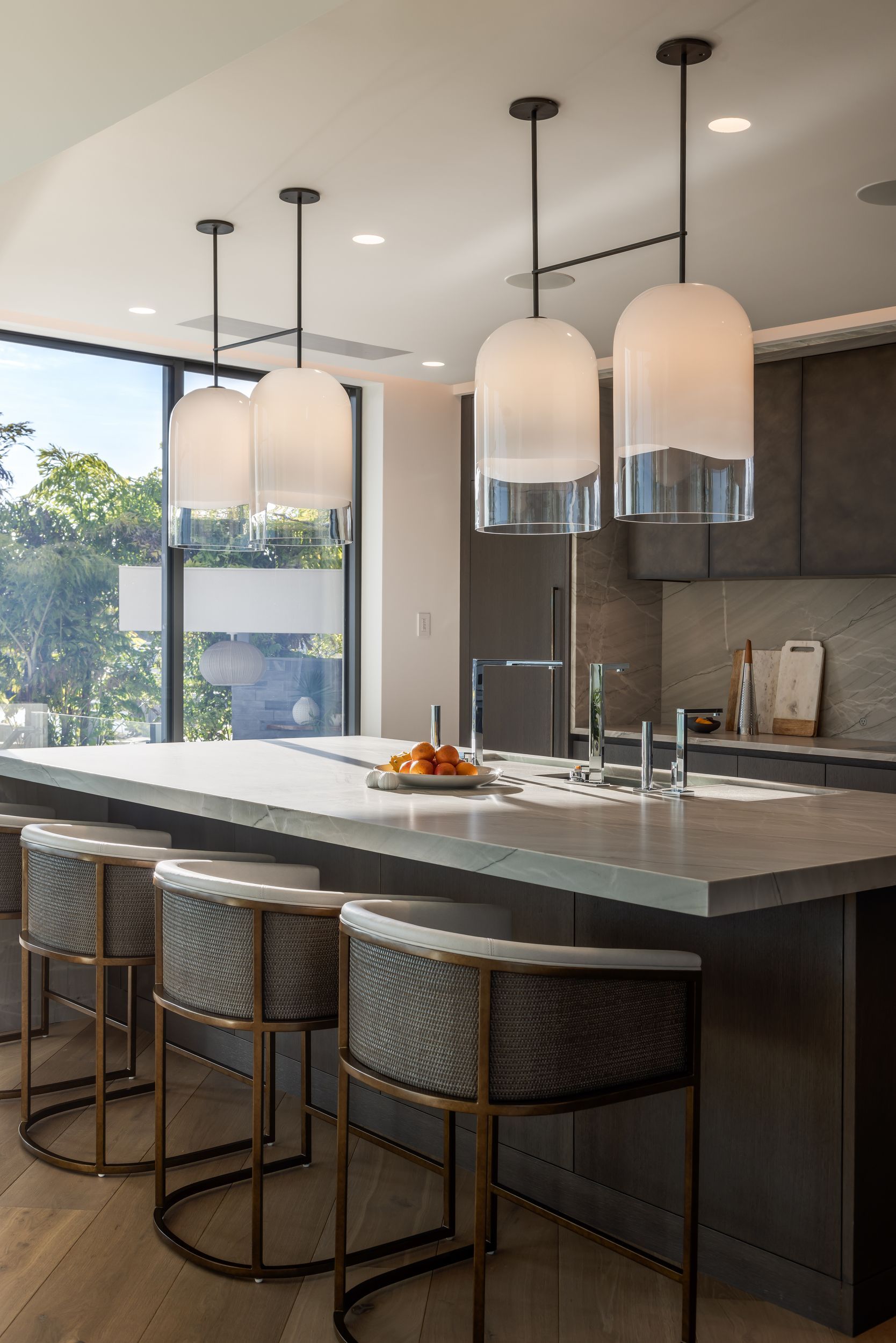 Modern kitchen with island, pendant lights, and woven bar stools. Neutral tones, large window.