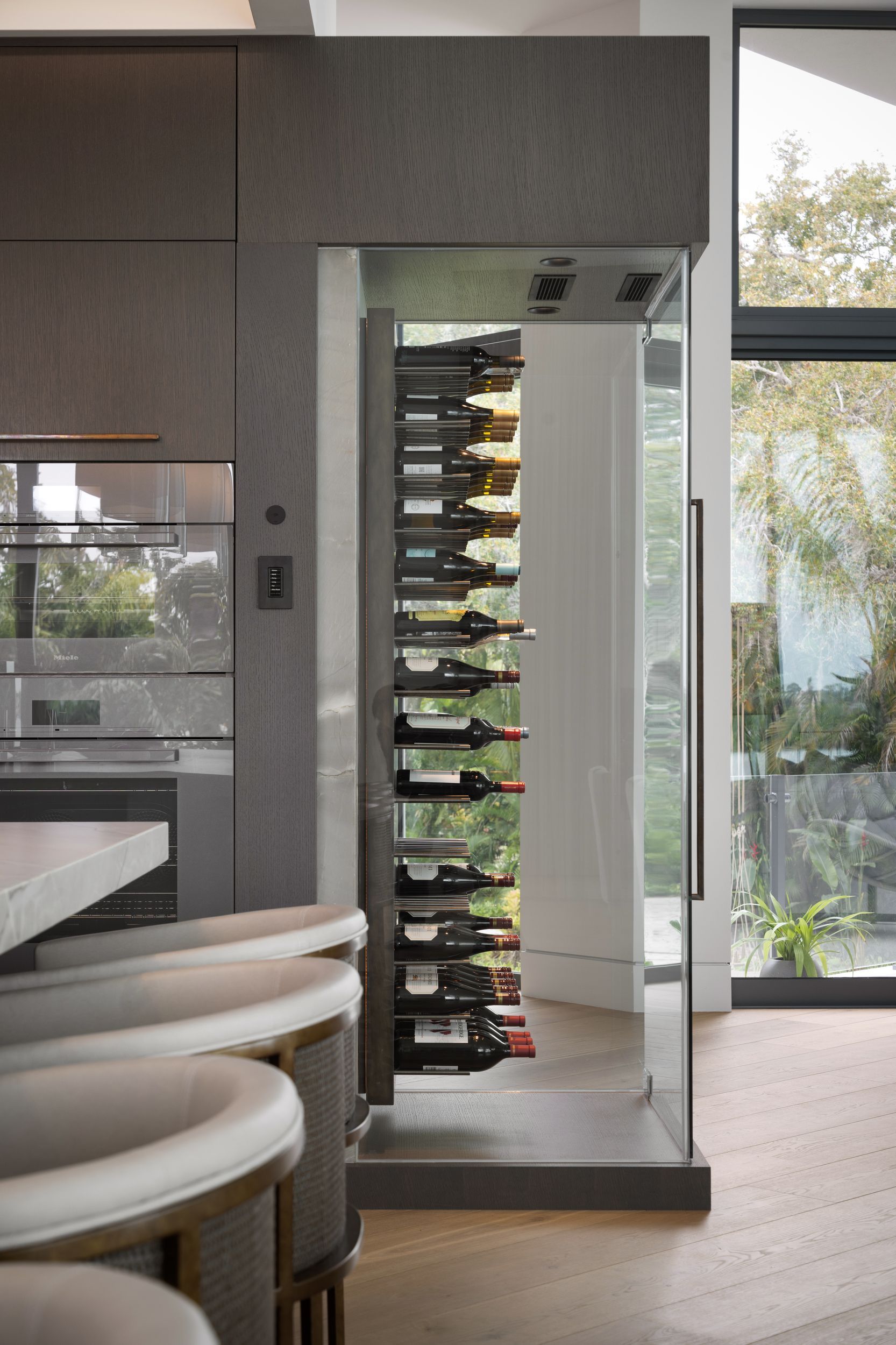 Modern wine cellar with glass door, inside a gray stone column, next to a window.