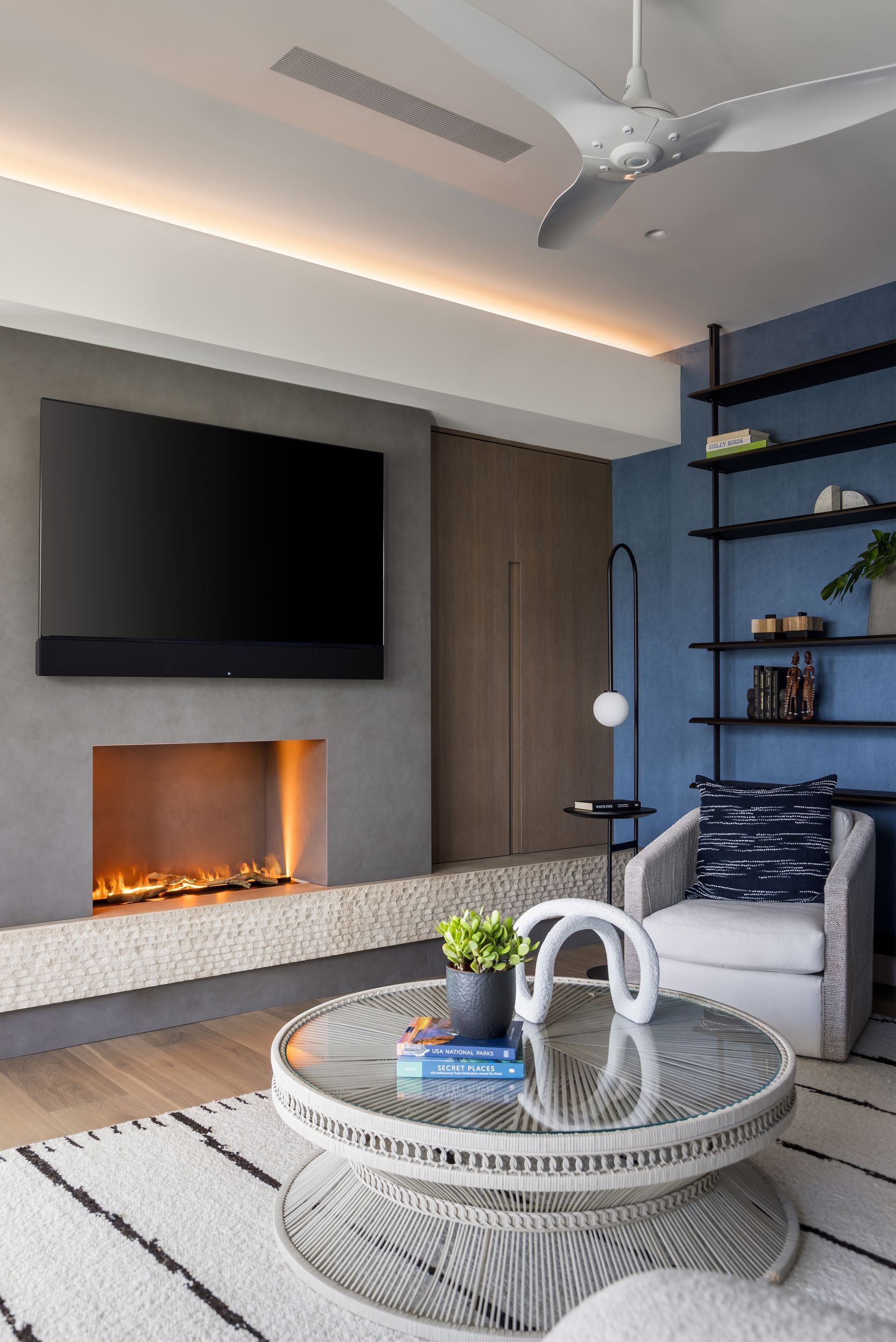 Modern living room with fireplace, TV, and blue accent wall with shelving and armchair.