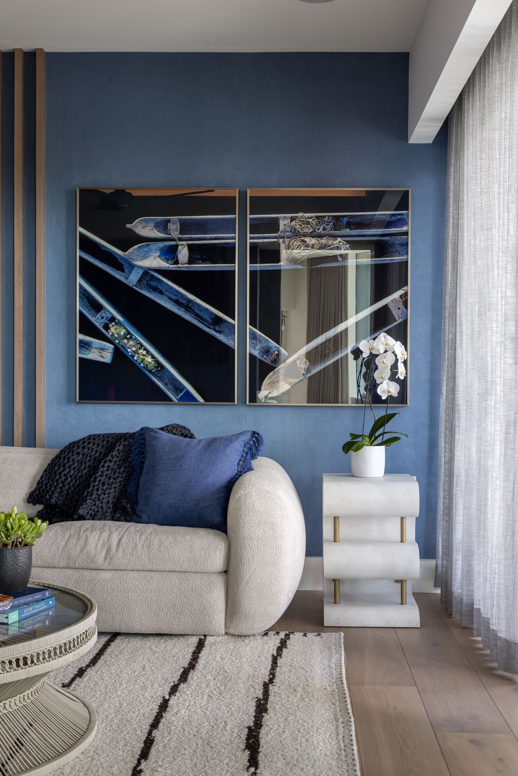 Living room with blue wall, artwork, textured sofa, rug, and side table with flowers.