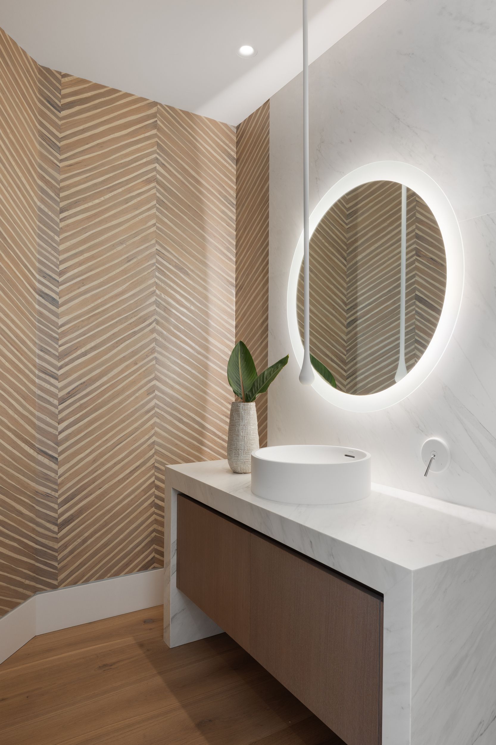 Modern bathroom with round backlit mirror, vessel sink, and textured tan walls.