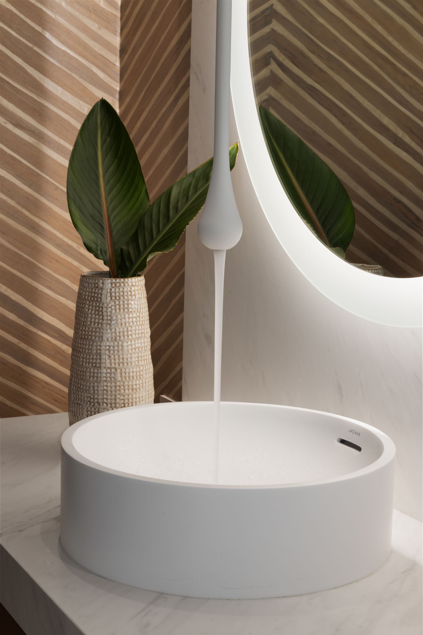 White modern sink with water flowing. Plant and decorative wall behind.