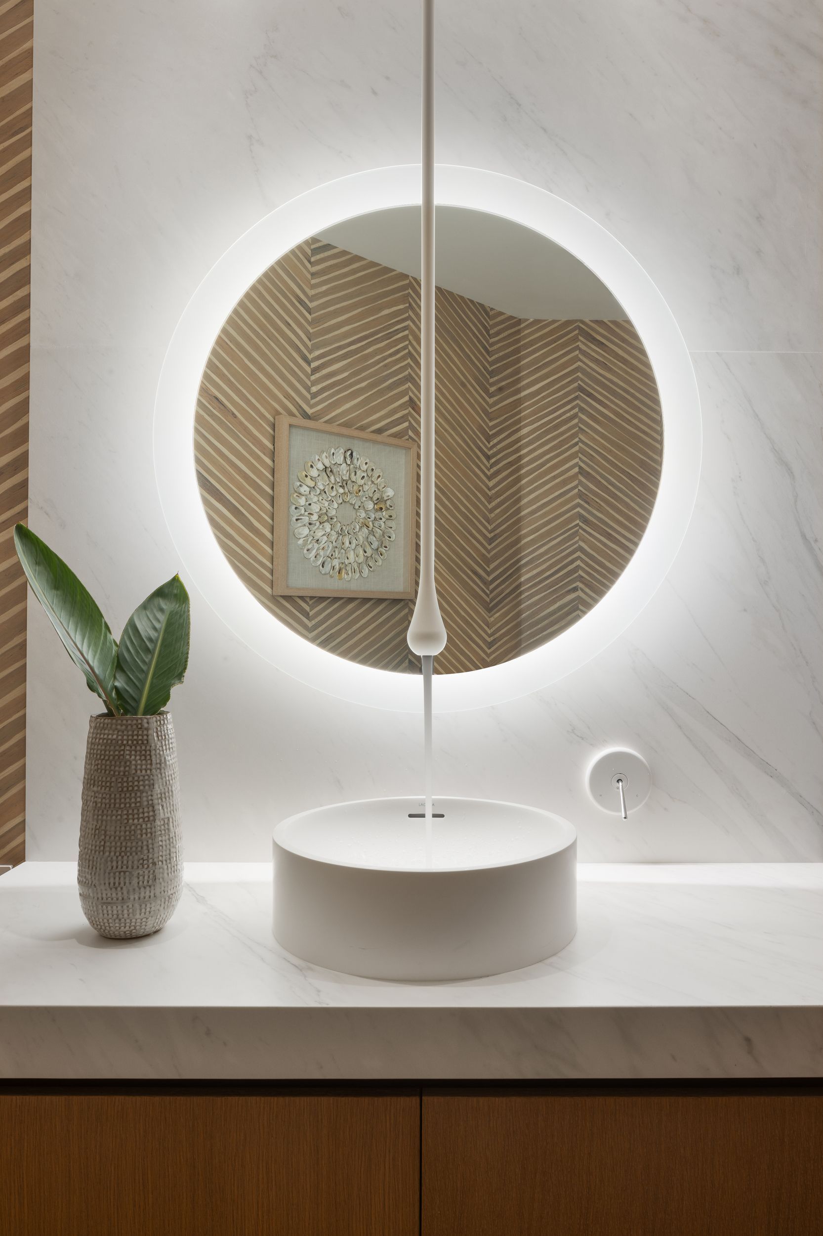 Bathroom with round mirror, overhead light, white sink, and decorative plant.