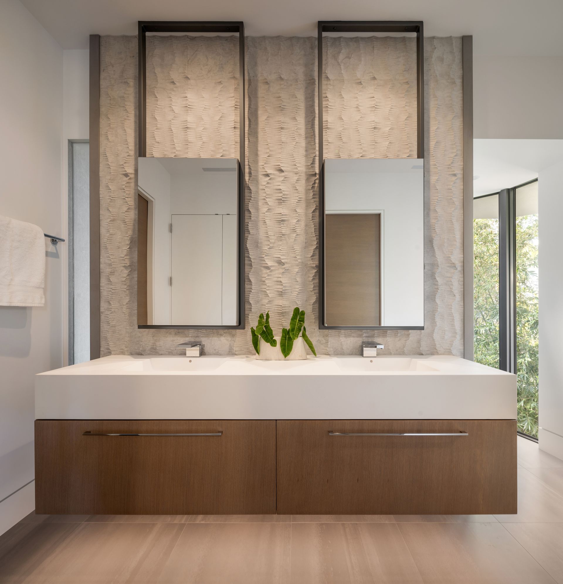 Modern bathroom with double vanity, stone wall, framed mirrors, and wood cabinetry.
