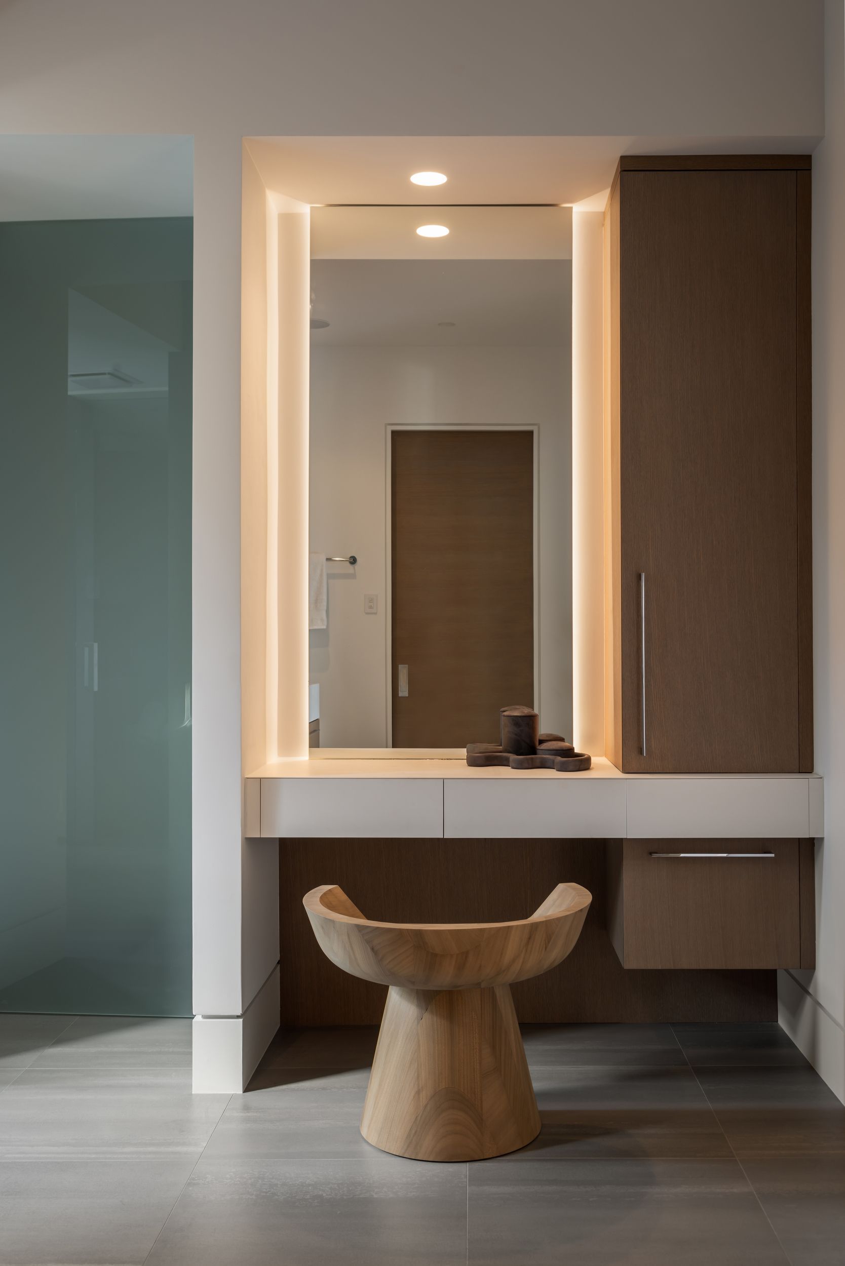 Vanity area with a wooden stool, a large mirror with integrated lighting, and a beige cabinet.