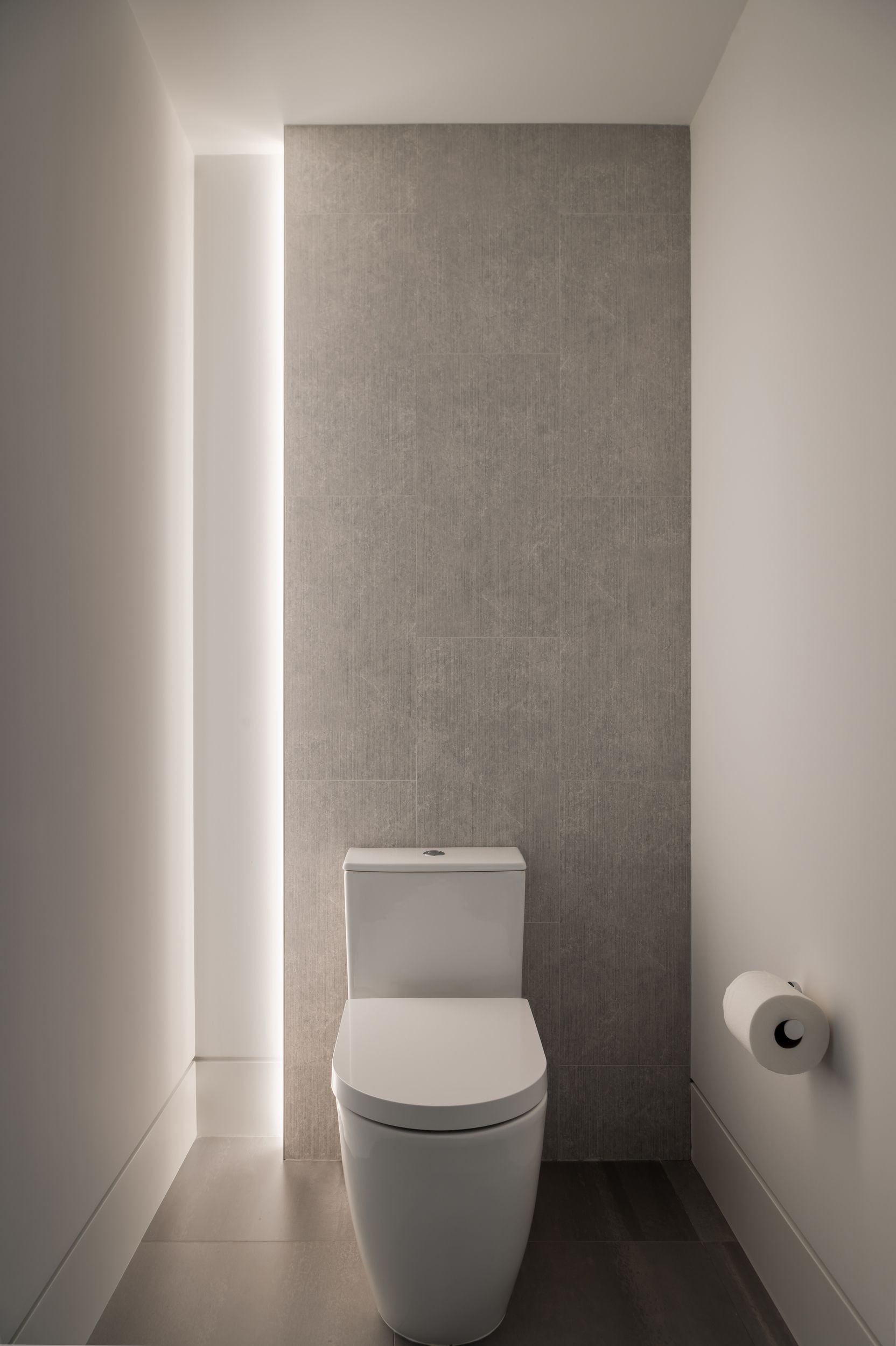Modern bathroom with a white toilet against a textured gray tile wall.  LED lighting on the side.