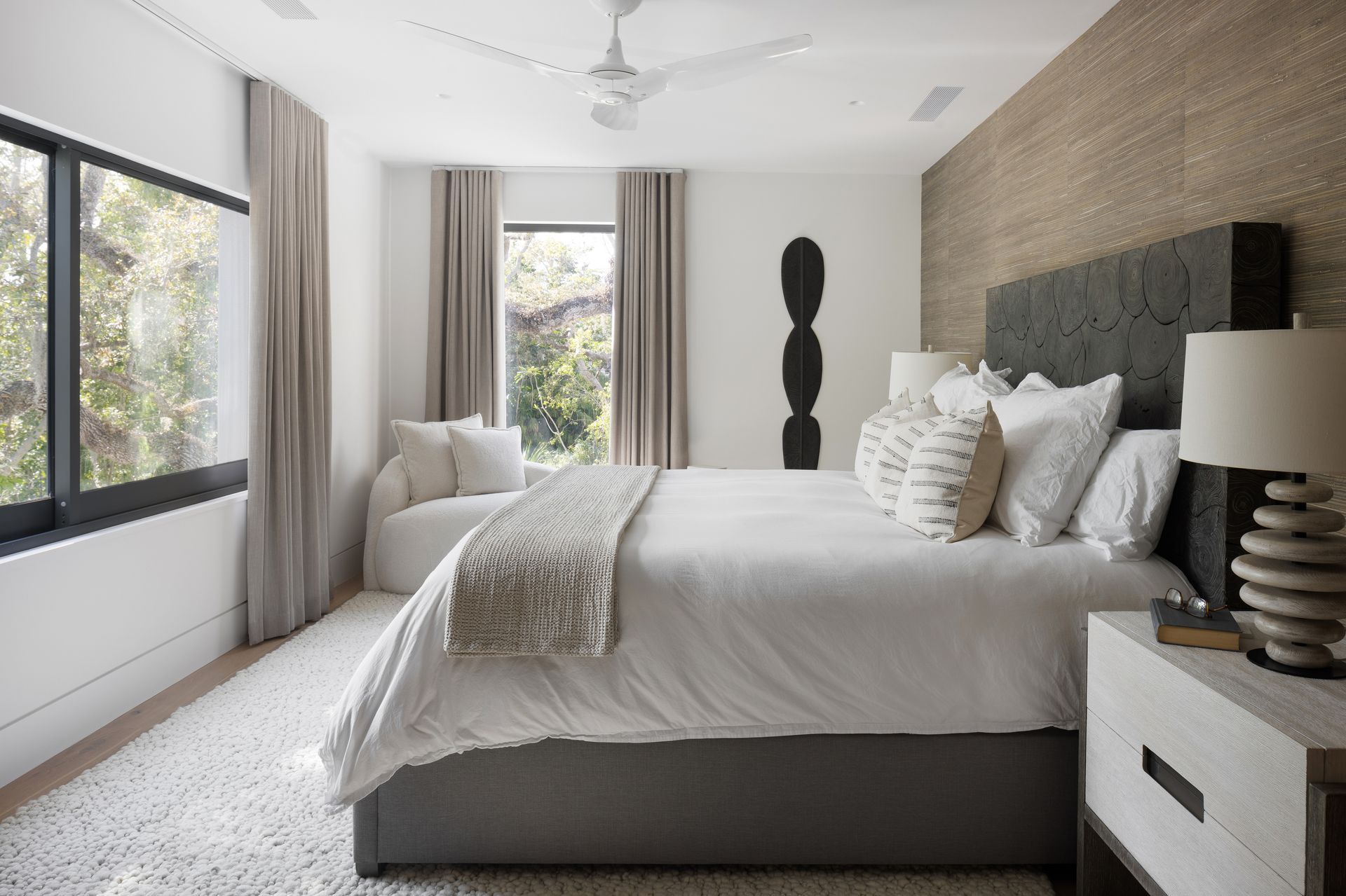 Bedroom with bed, neutral colors, textured headboard, window with curtains.