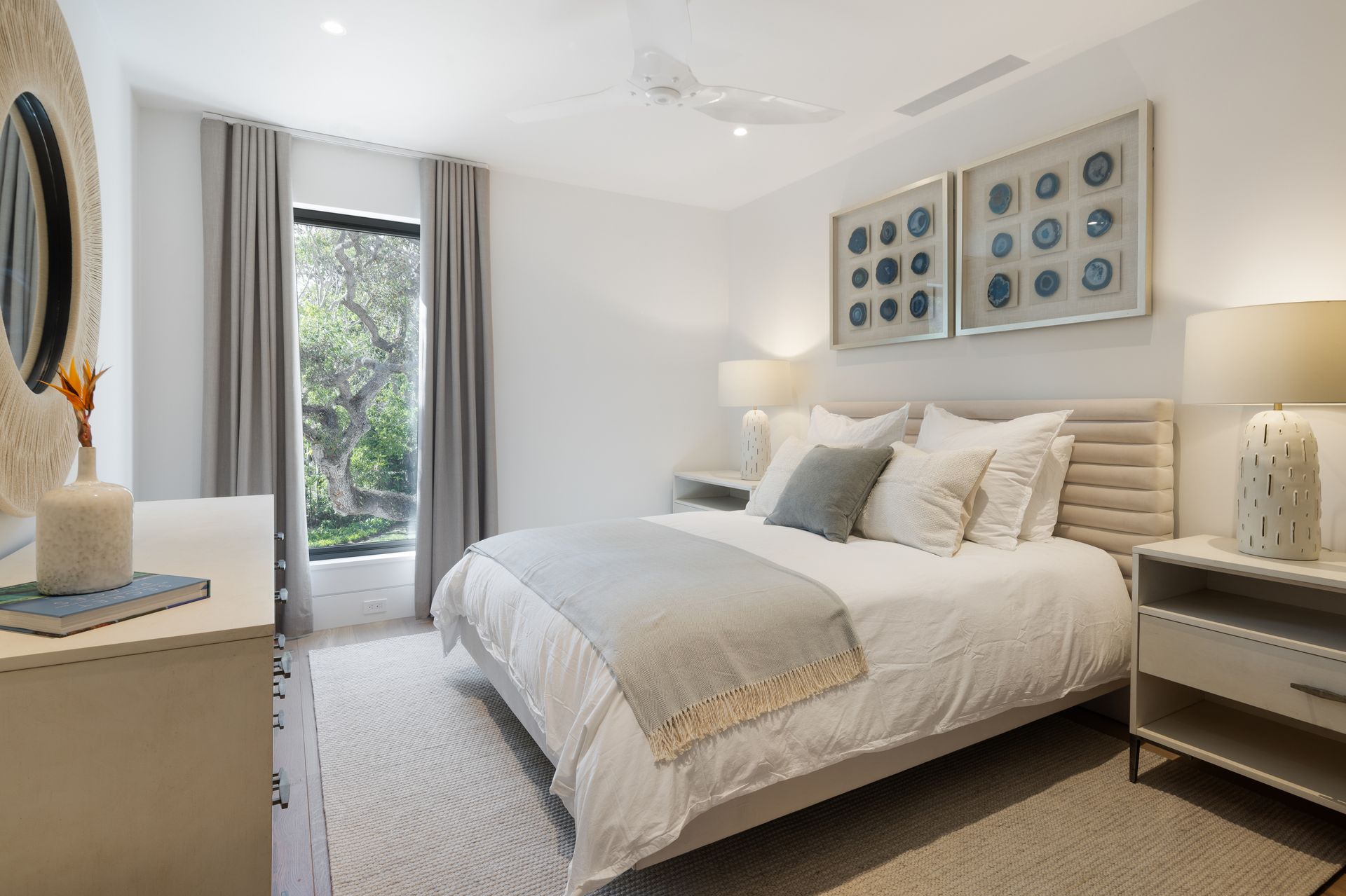 Bedroom with white walls, bed, window, nightstands, artwork, and a rug.