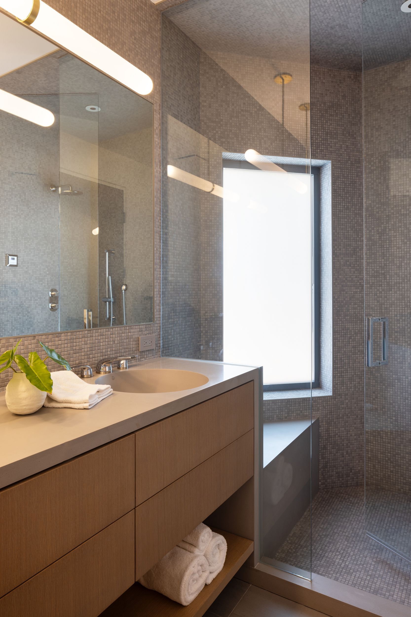 Modern bathroom with stone tile walls, wooden vanity, and glass shower.