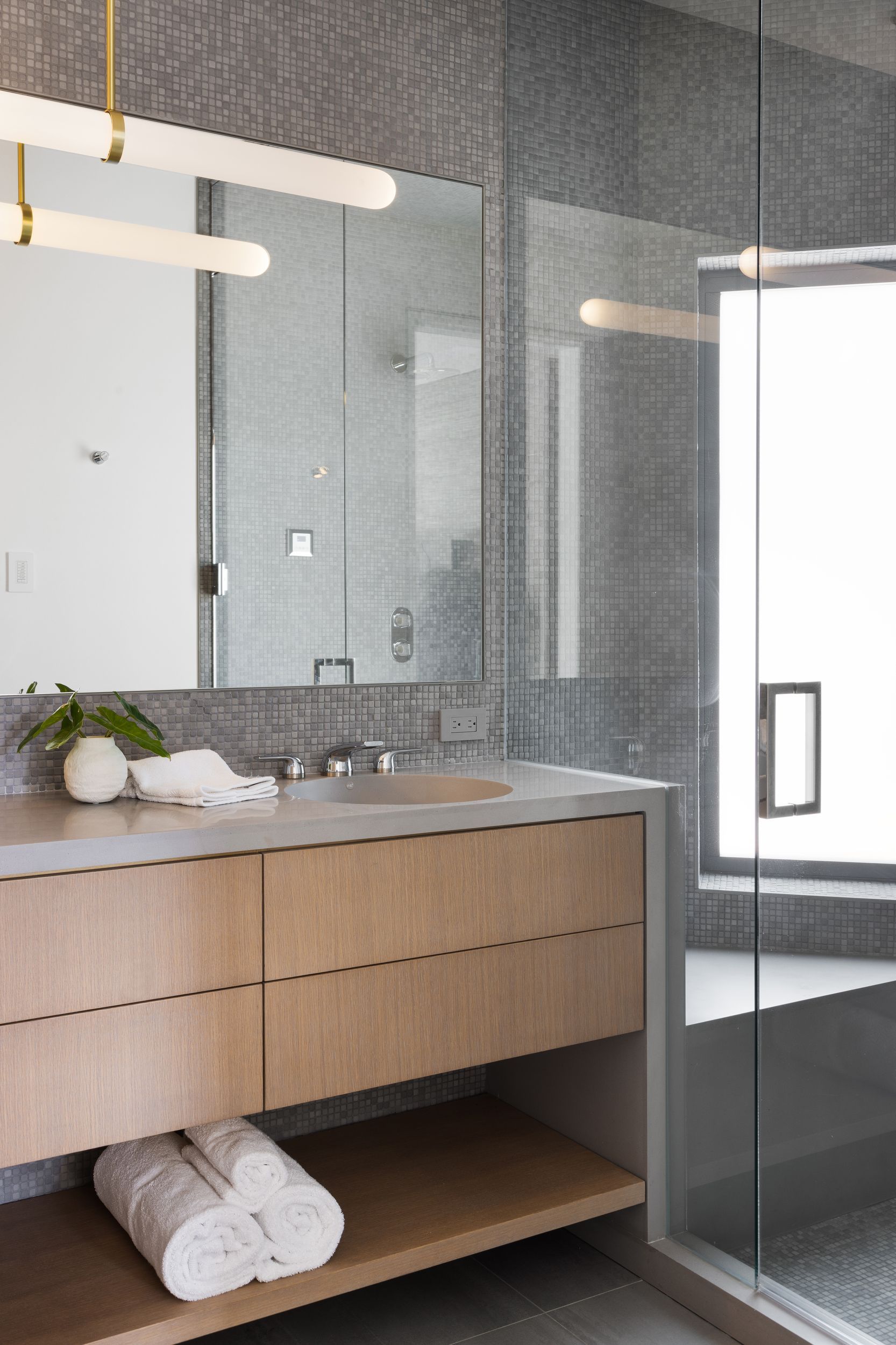 Modern bathroom with wood vanity, large mirror, glass shower, and gray tile.