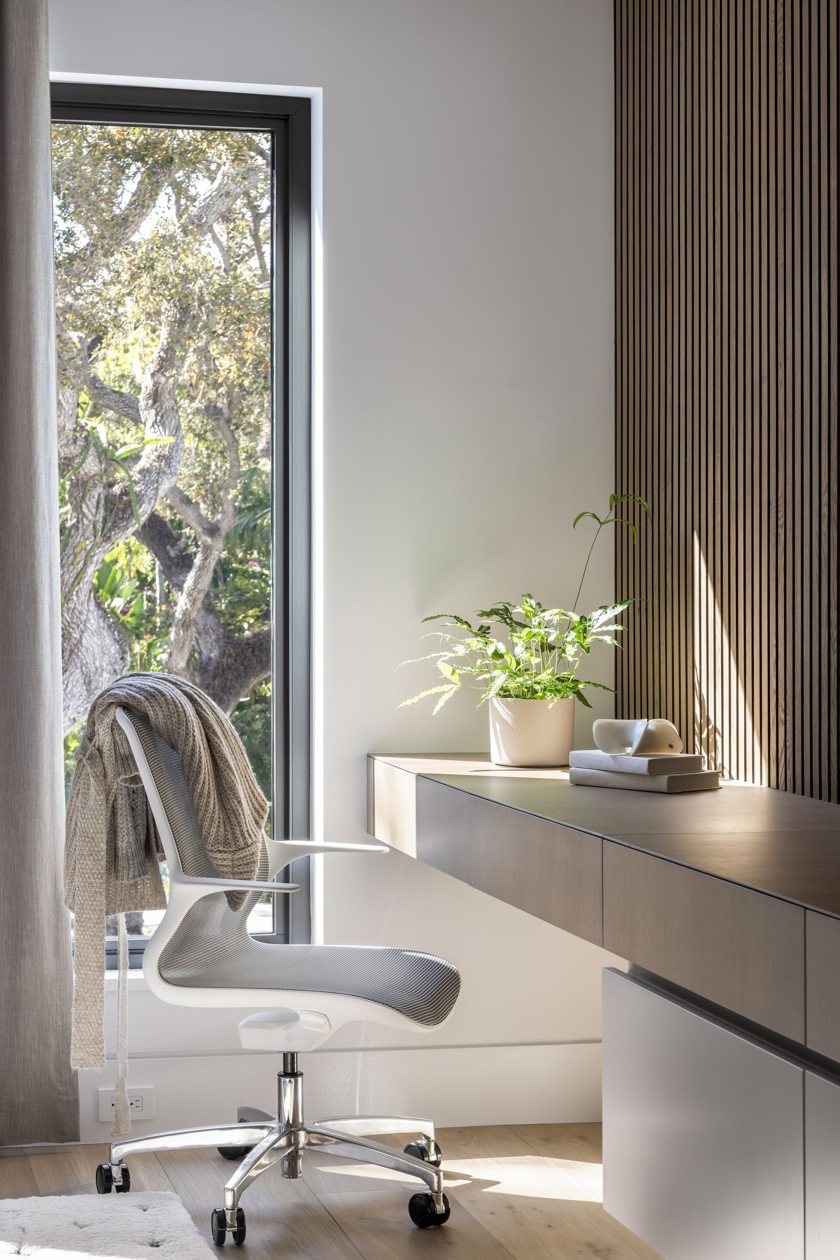 Modern home office with desk, chair, window view of trees, and plants.