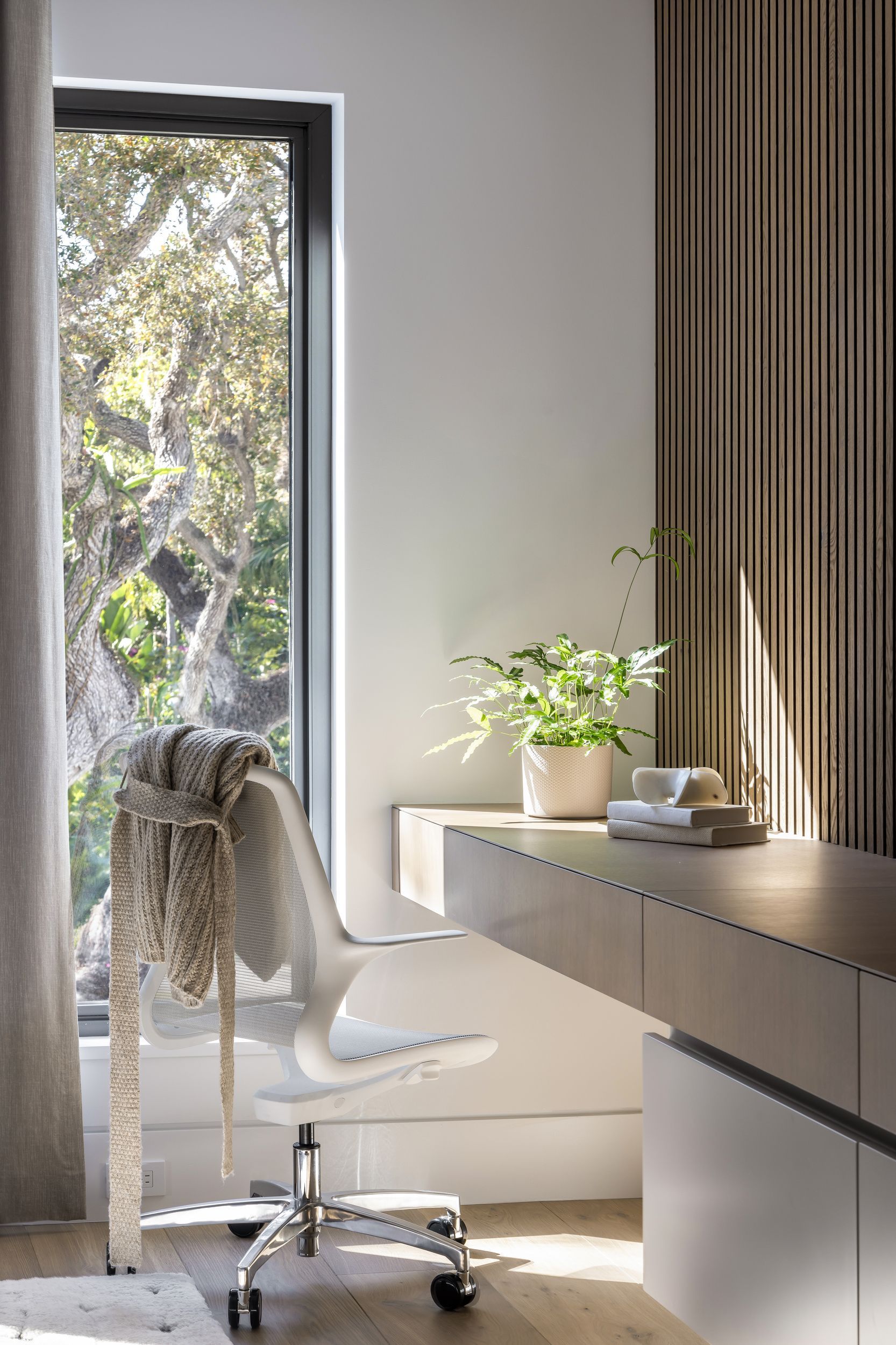 Modern office space with a built-in desk, ergonomic chair, and window overlooking trees.