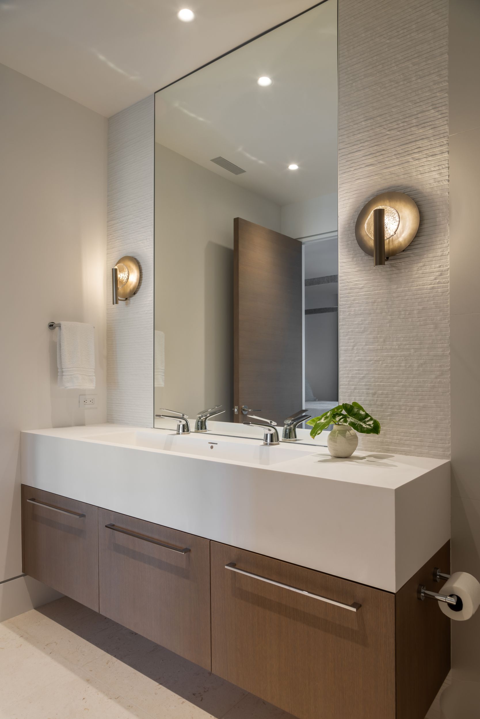 Modern bathroom with floating wooden vanity, large mirror, sconces, and white countertop.