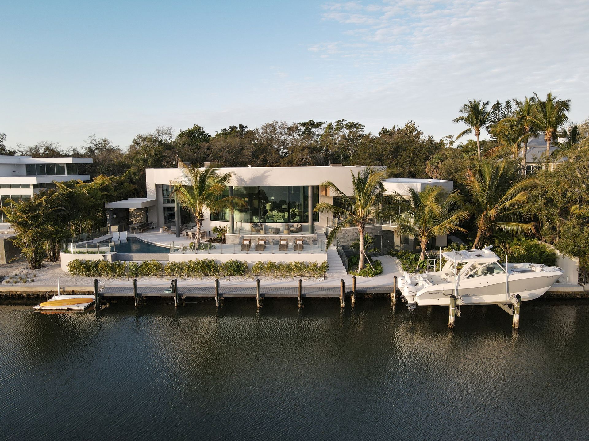 Modern waterfront home with pool, docked boat, and lush tropical landscaping.