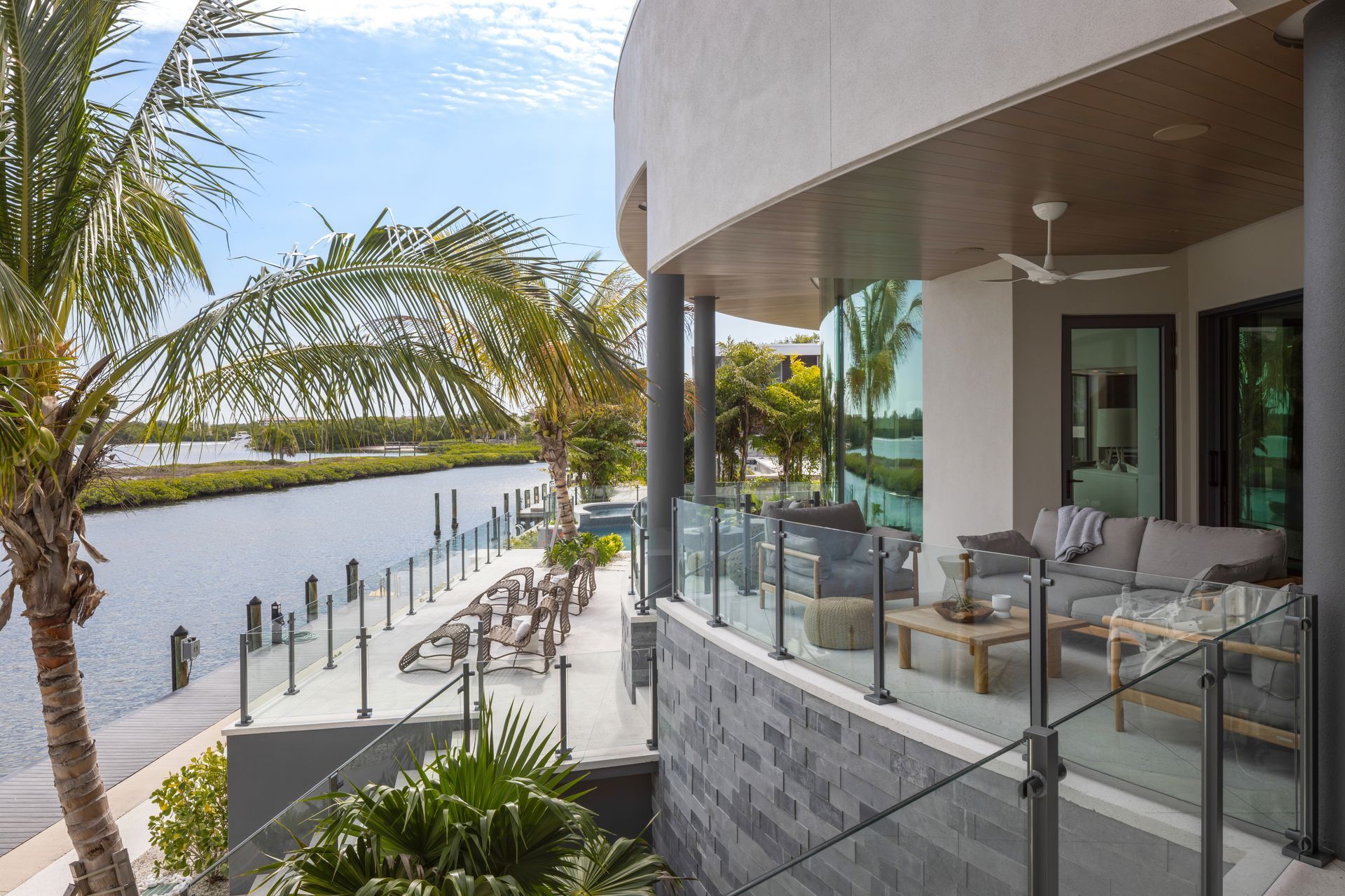 Waterfront home with deck, glass railing, canal view, palm trees, and outdoor seating.