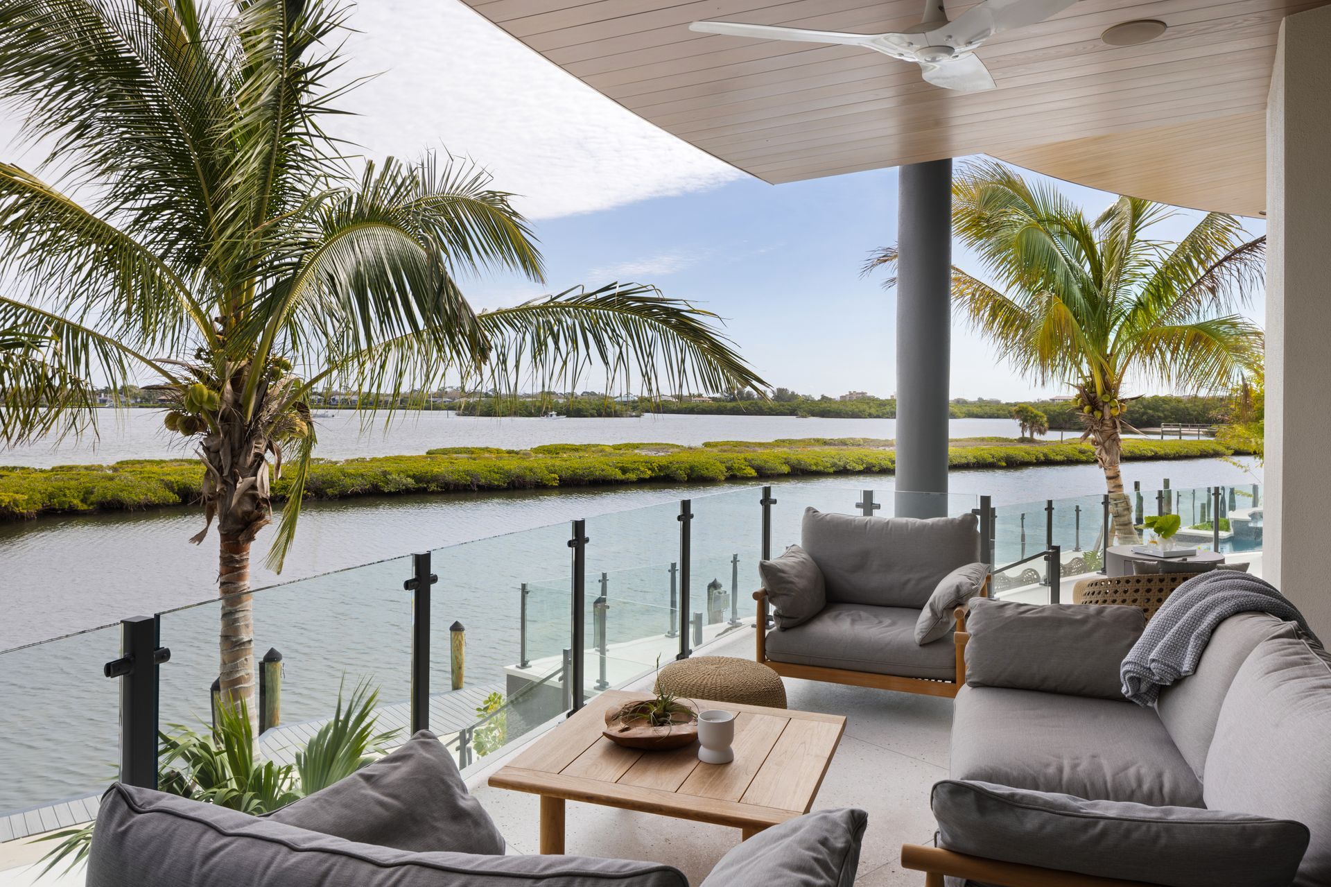 Outdoor patio with gray furniture overlooking a canal with palm trees.