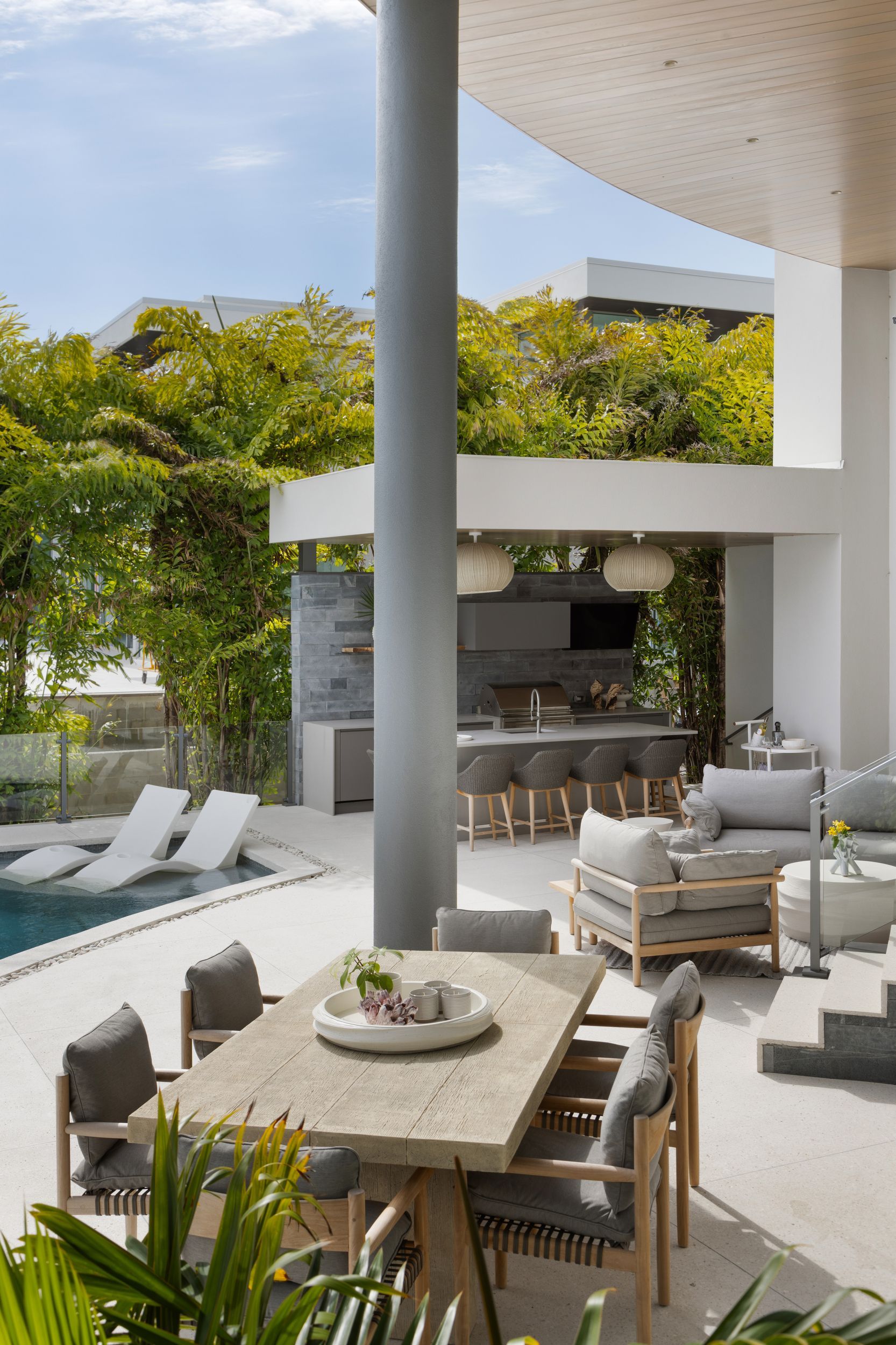 Outdoor patio with dining and lounge areas near a pool; light gray and neutral tones; sunny day.