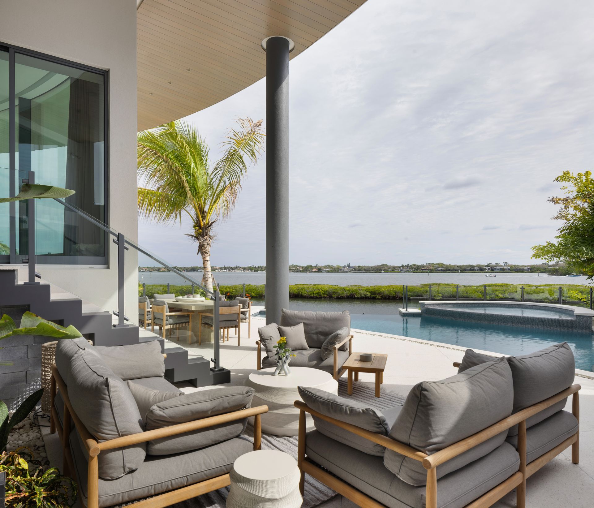 Outdoor patio with gray couches, pool, and water view.
