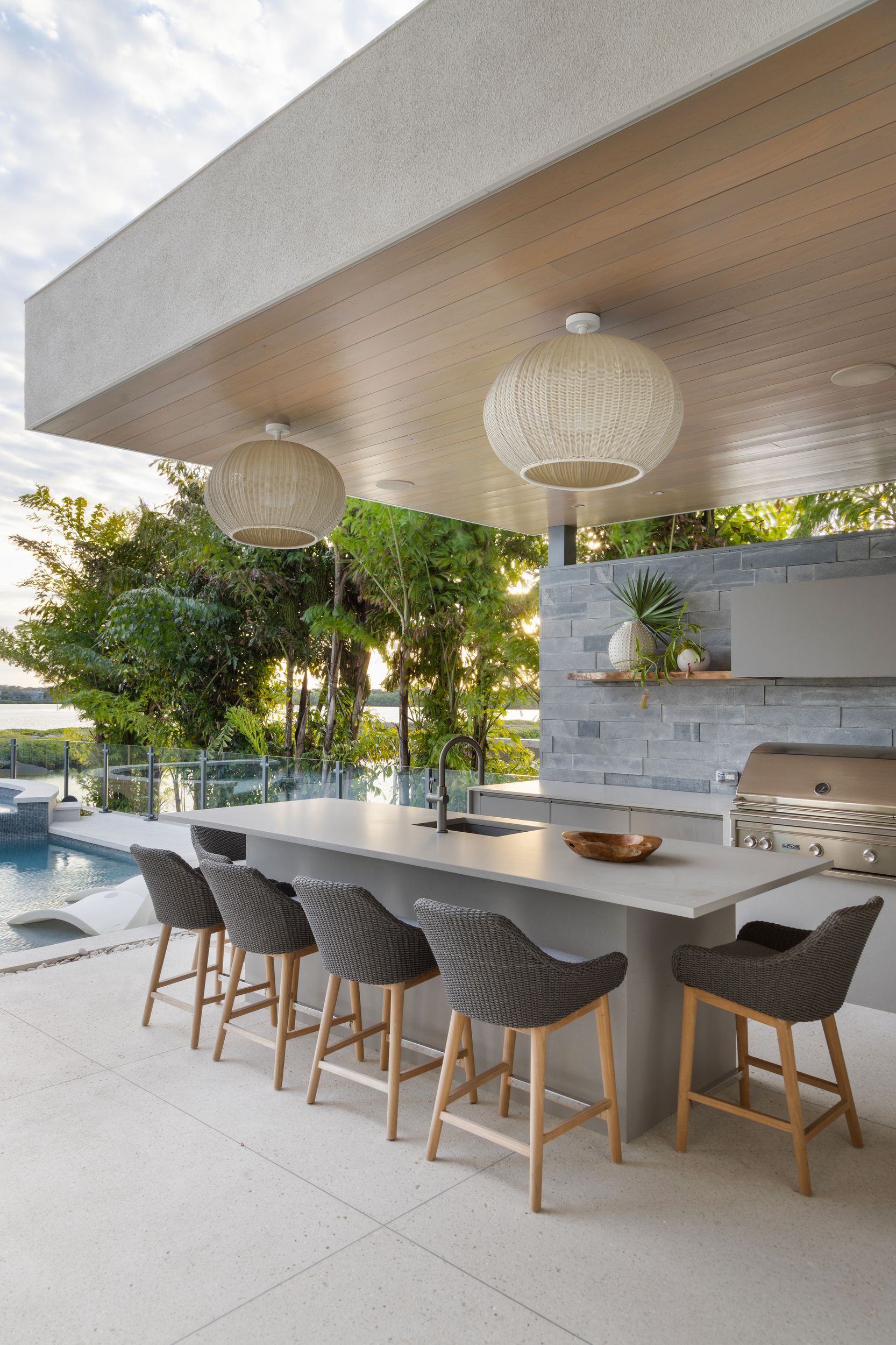 Outdoor kitchen with a counter, stools, and built-in grill under a covered area.