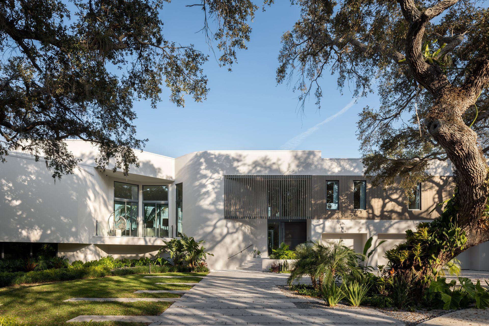 Modern white house with gray accents, pathway, and lush landscaping under a blue sky.