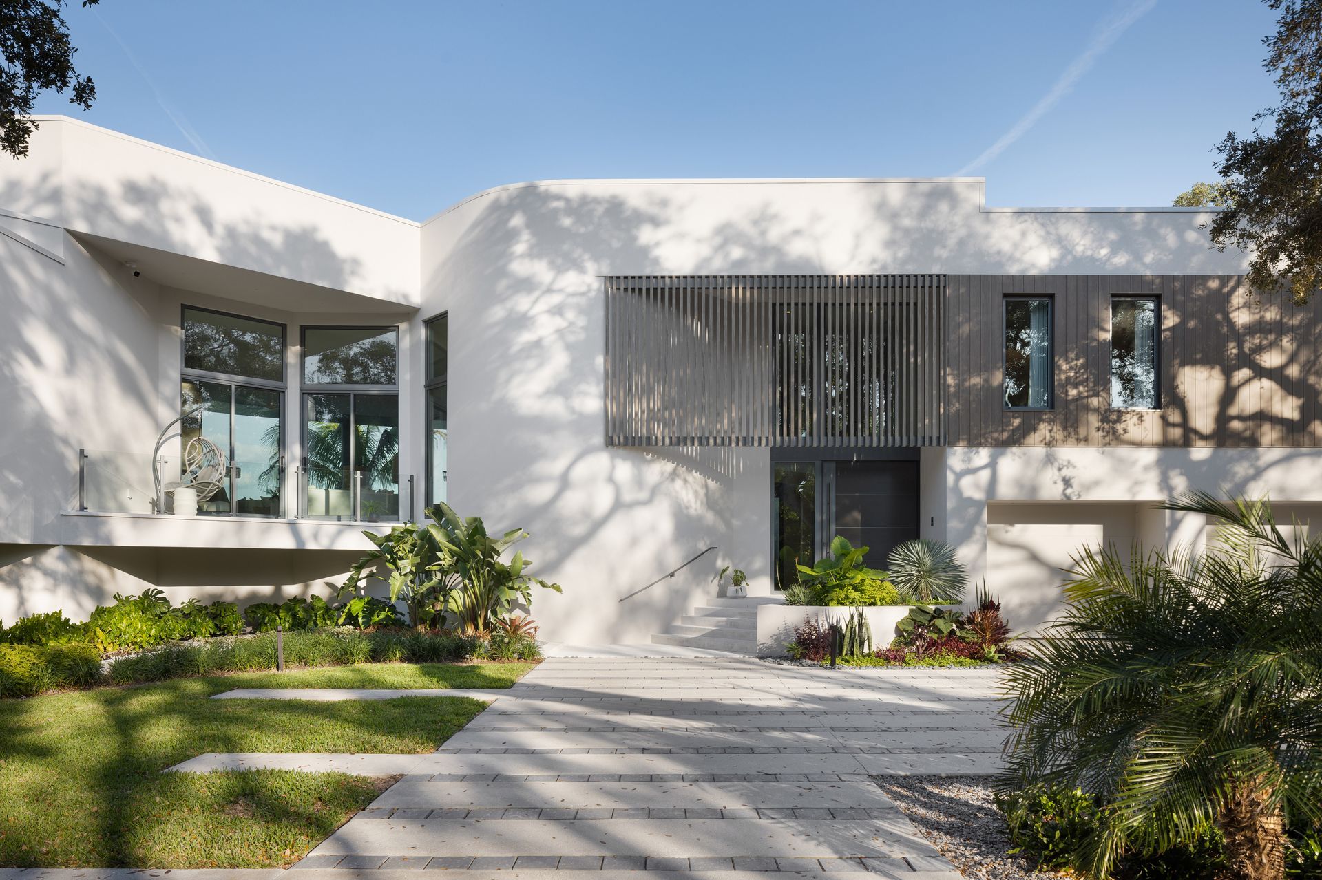 Modern white house with a landscaped yard and a paved walkway.