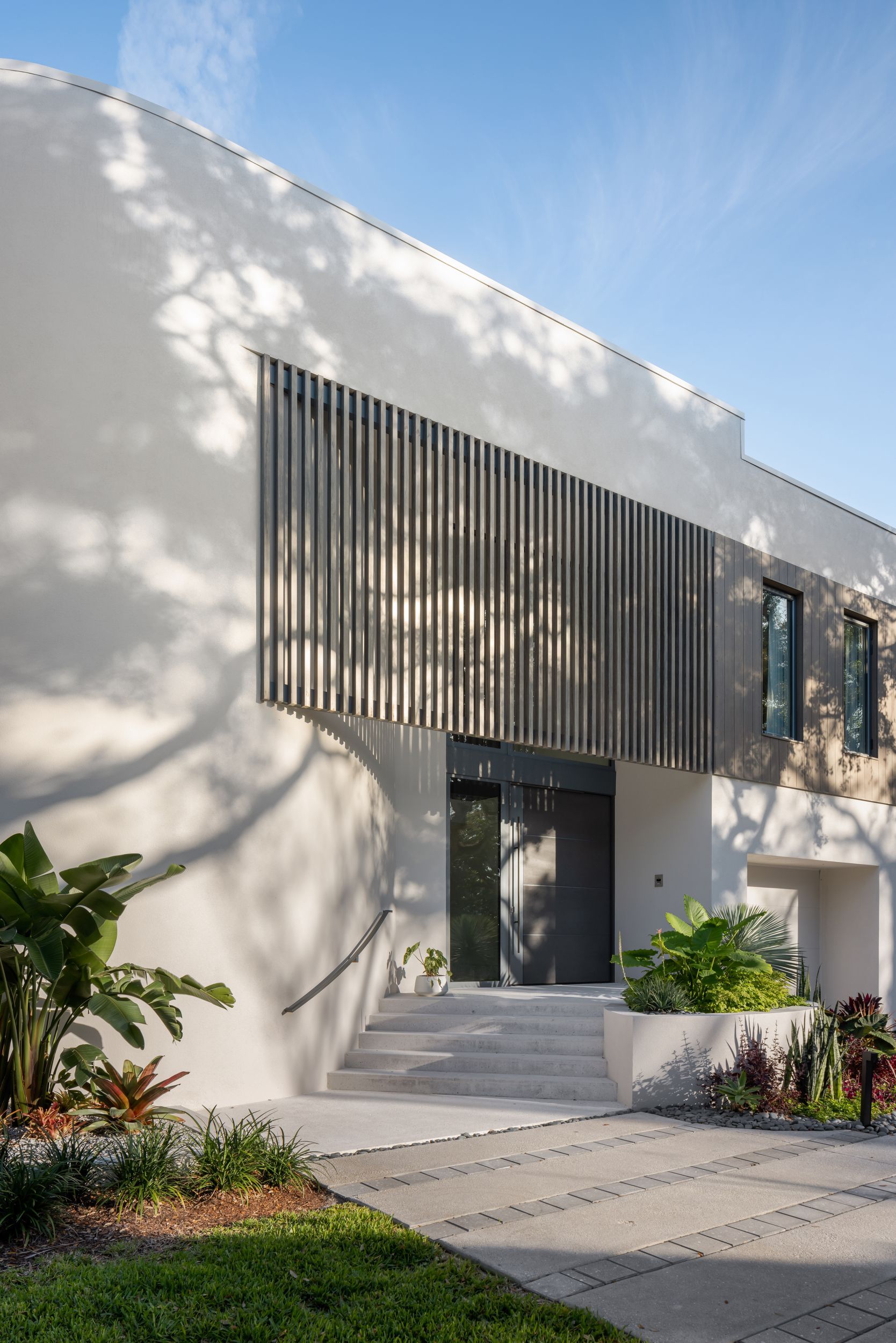 Modern building with gray wooden slats, concrete steps, and landscaping.