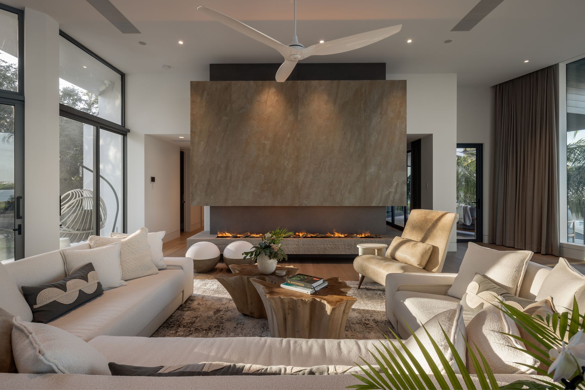 Modern living room with fireplace, white couches, large windows, and neutral colors.