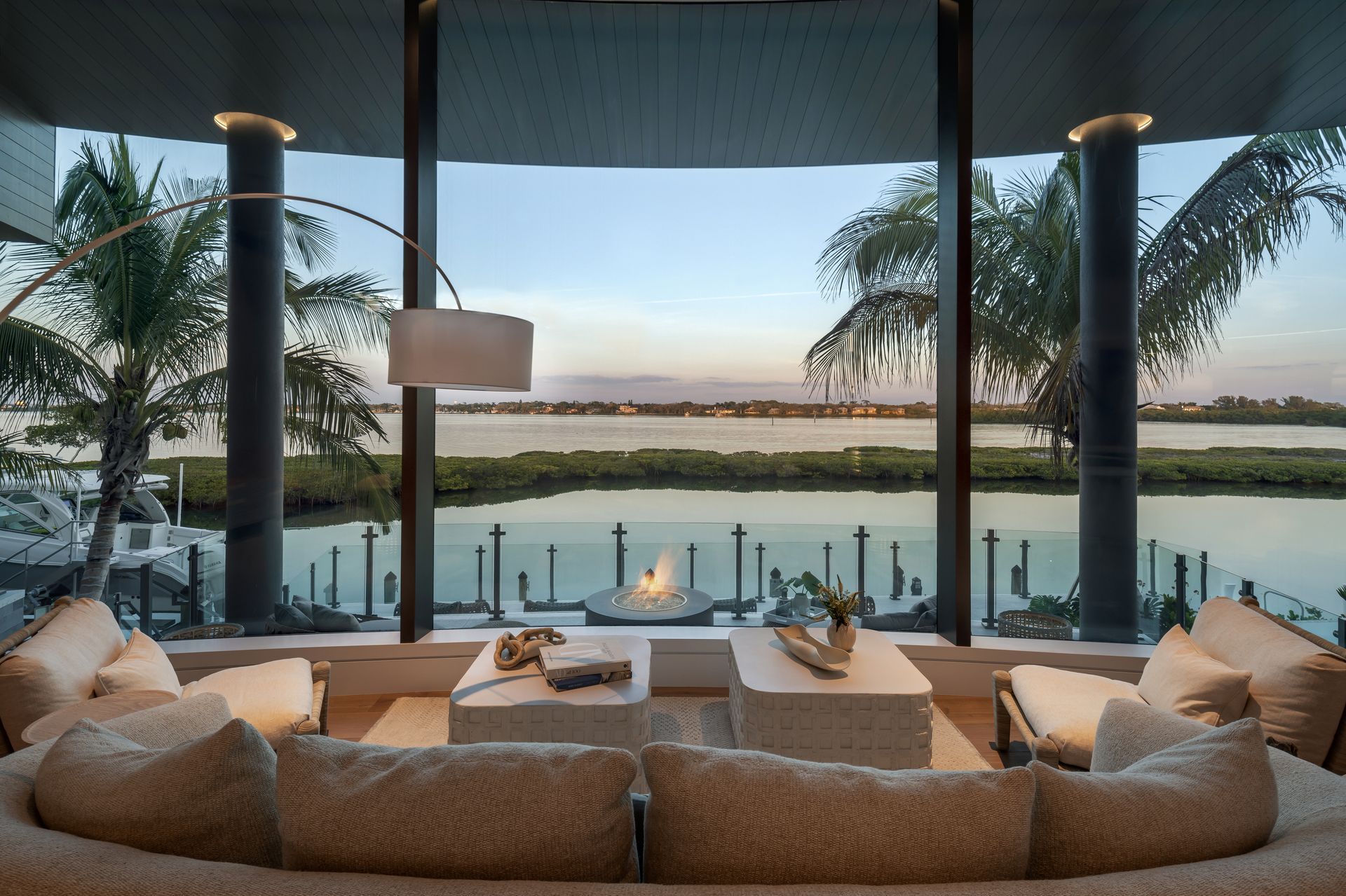 Living room with waterfront view, couches, coffee table, and palm trees.