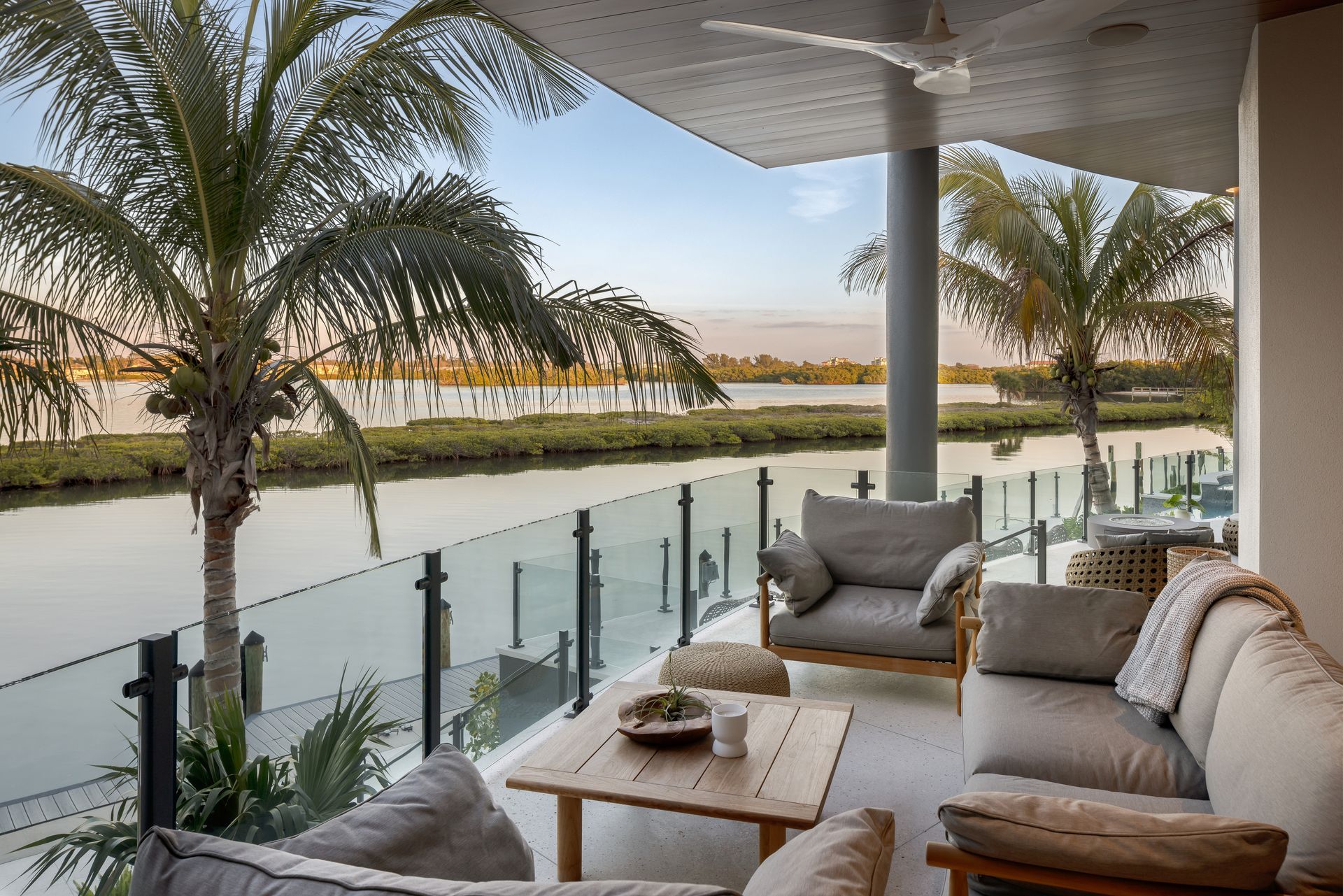 Outdoor patio with seating overlooking a waterway lined with greenery and palm trees.