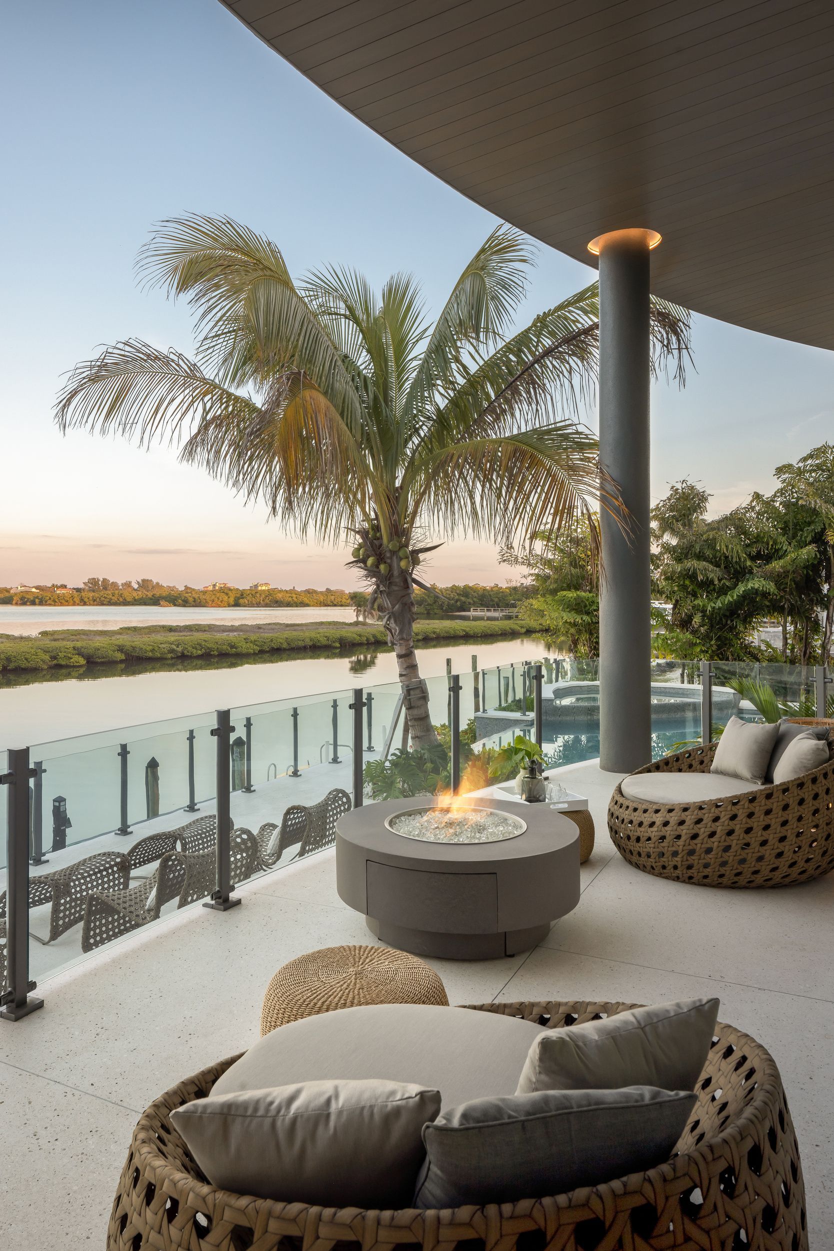 Outdoor patio with fire pit, wicker furniture, and water view at sunset.
